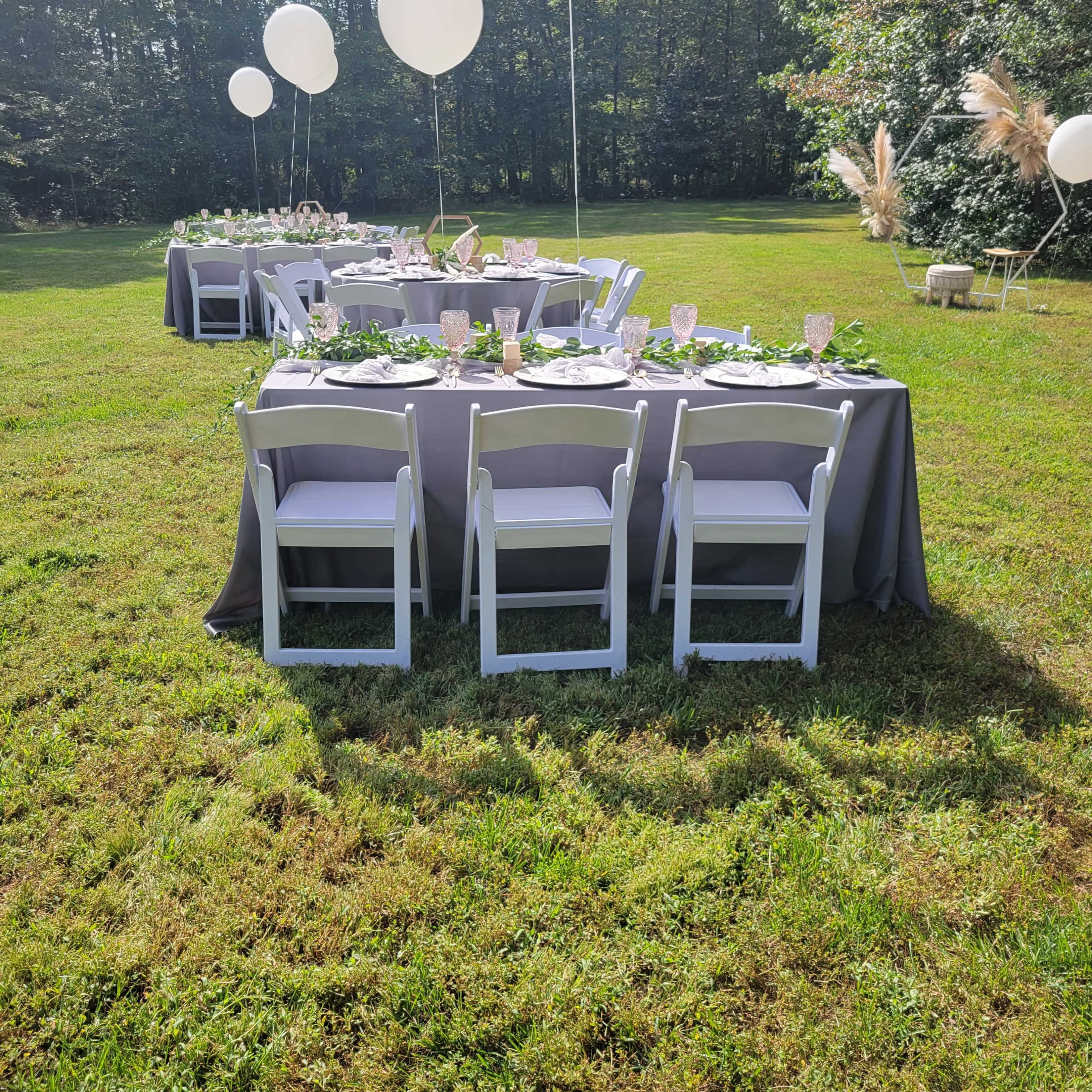 A neatly arranged outdoor dining setup features several tables covered with gray tablecloths, decorated with floral accents and topped with large white balloons.