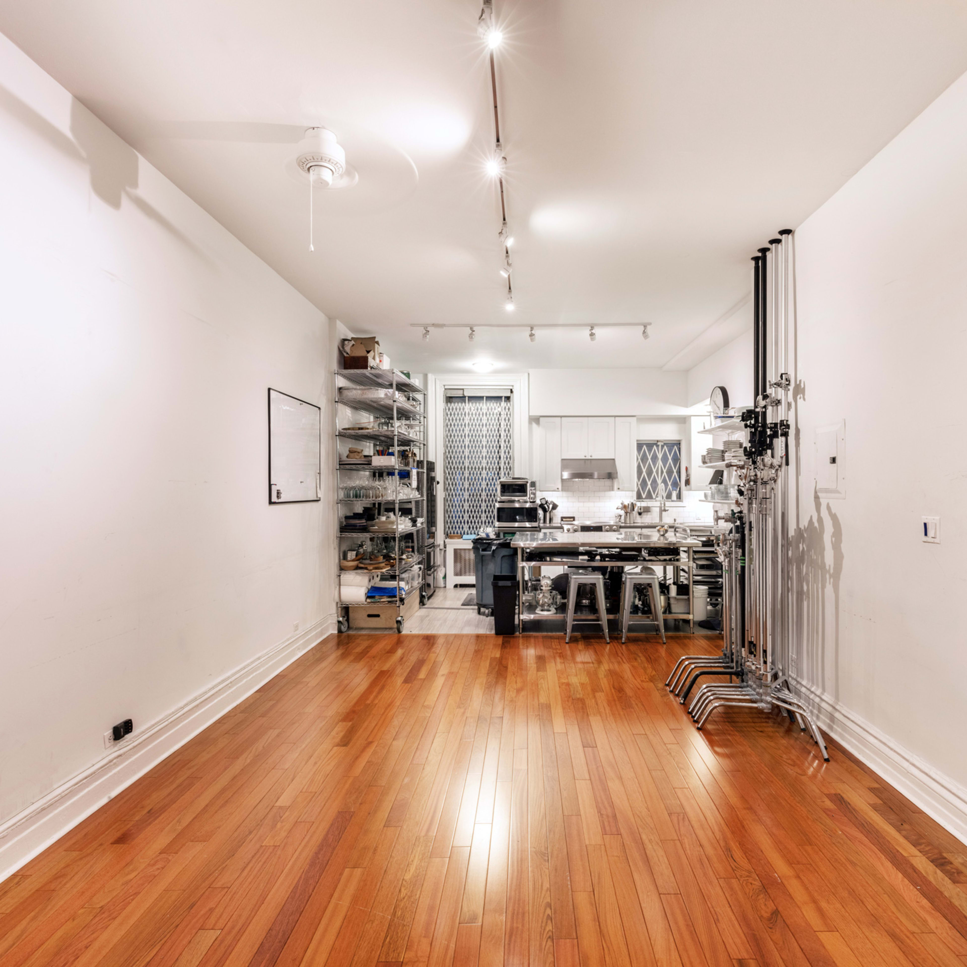 A spacious kitchen area with wooden flooring, stainless steel appliances, and shelves lining the walls.