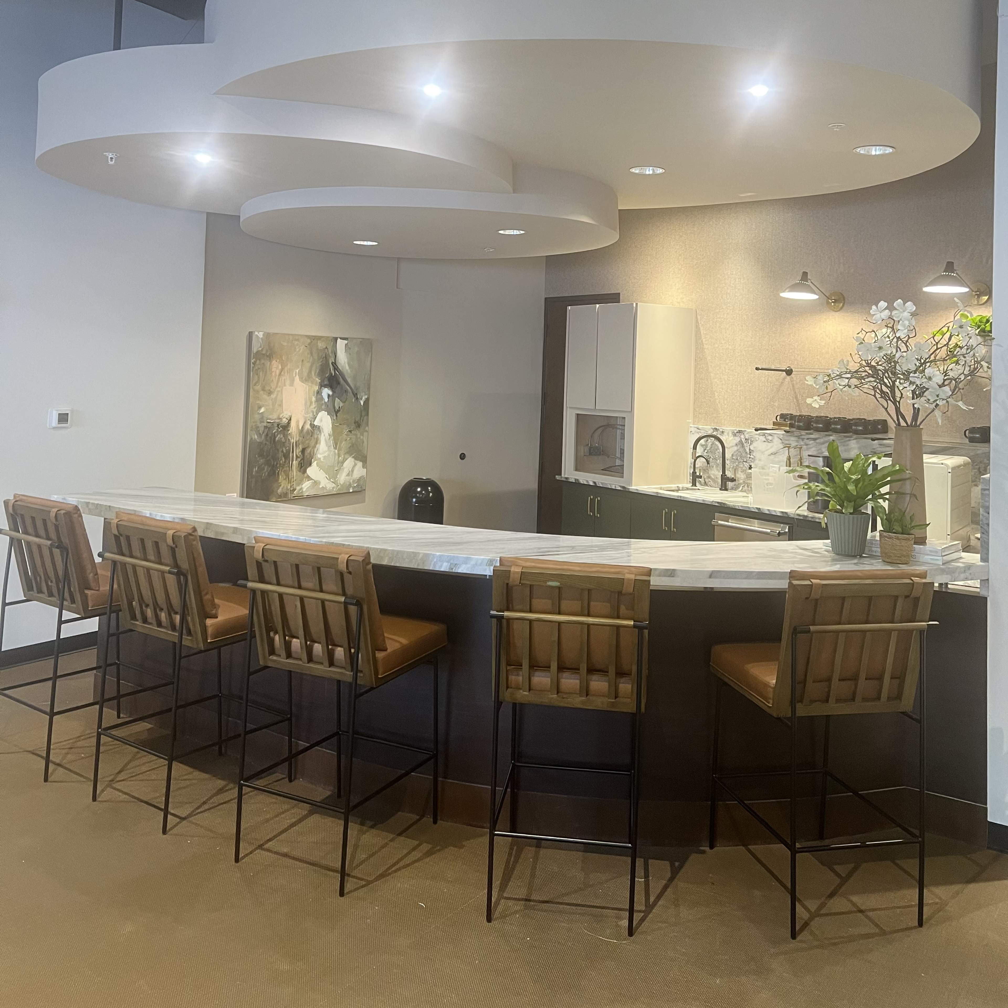 A modern kitchen bar area features a curved ceiling design, light fixtures, and seating with brown leather stools.