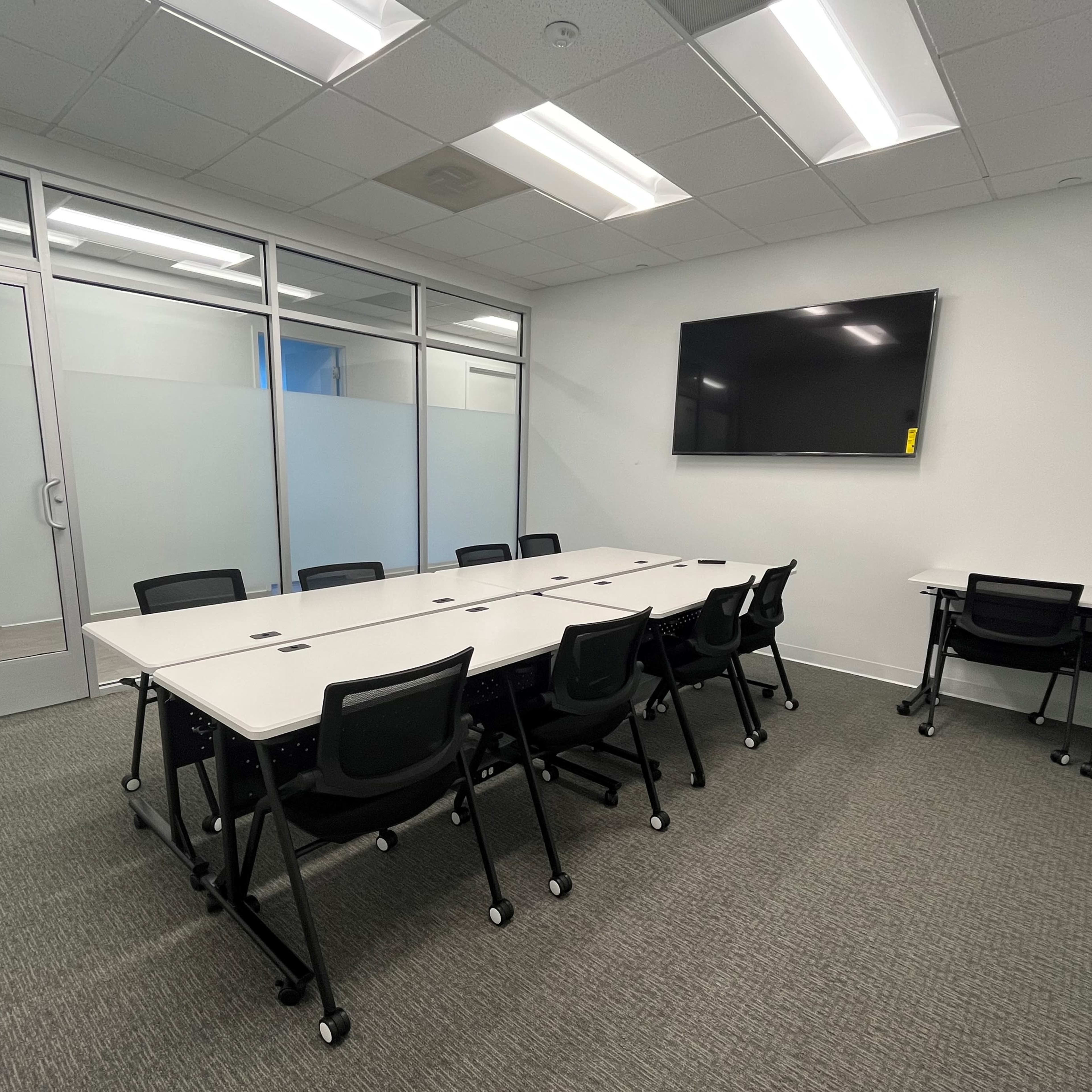 A conference room with a large table surrounded by chairs and a wall-mounted TV.
