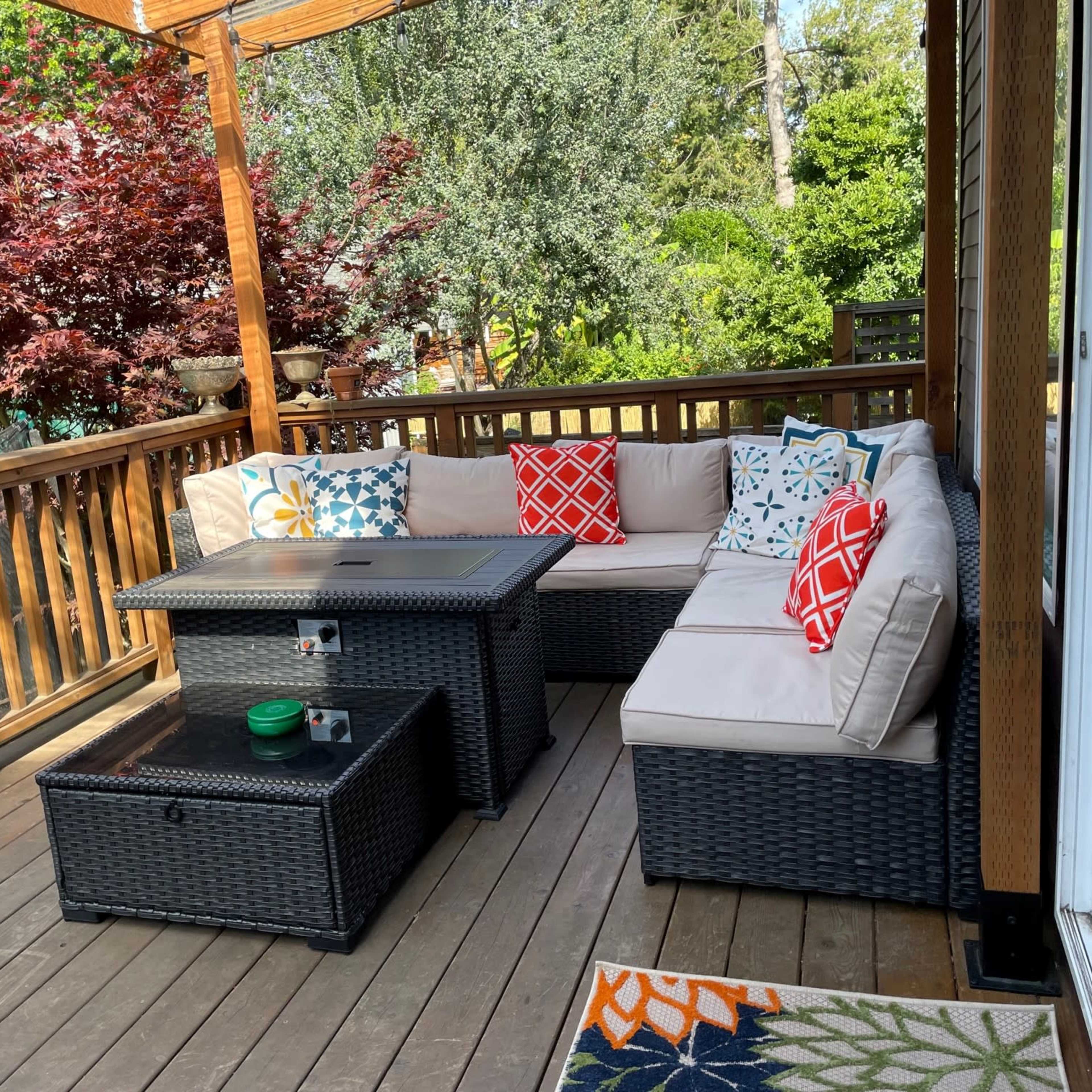 A seating area with a sectional sofa and coffee table, surrounded by greenery on a wooden deck.
