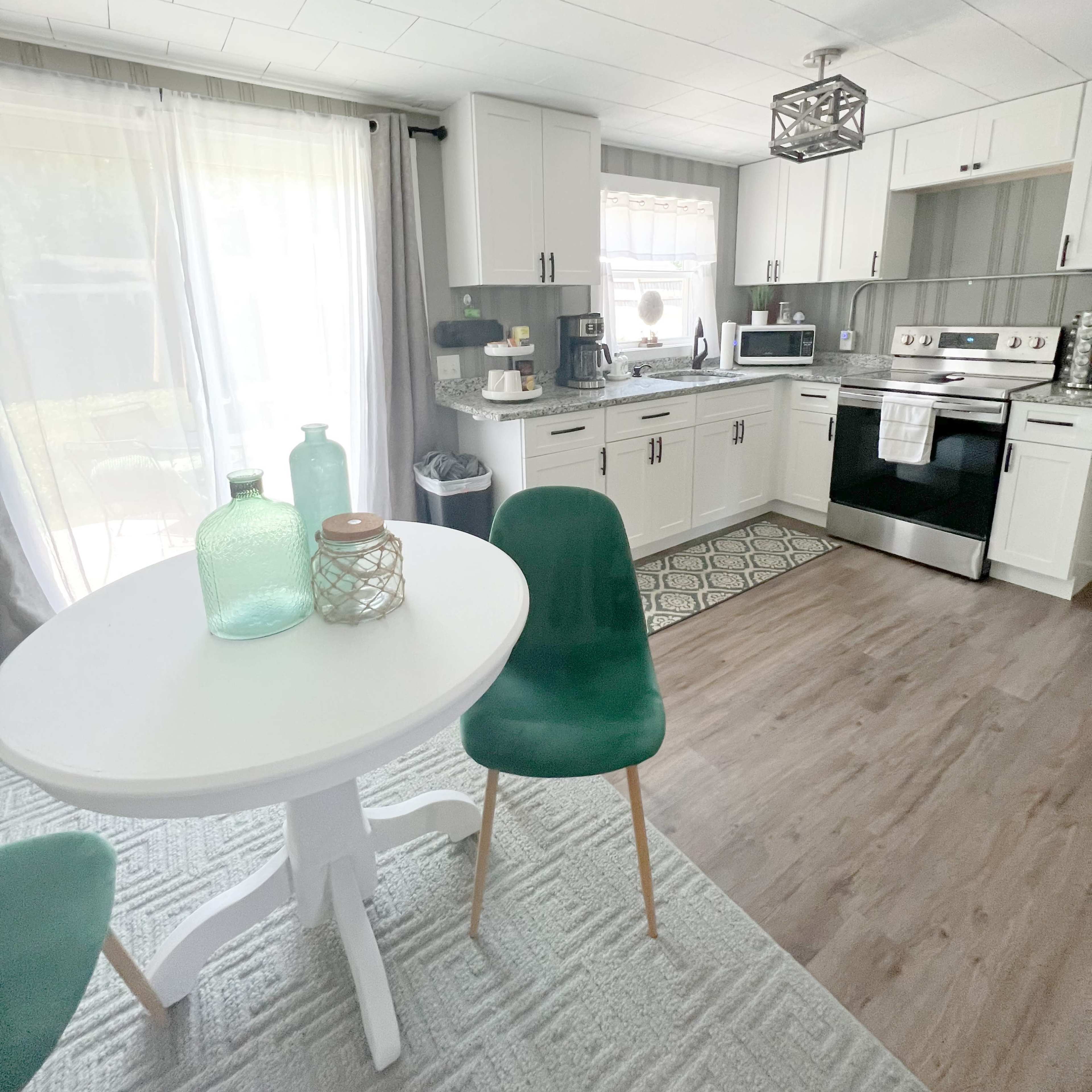 A bright kitchen features white cabinets, a black stove, and a round dining table with green chairs.
