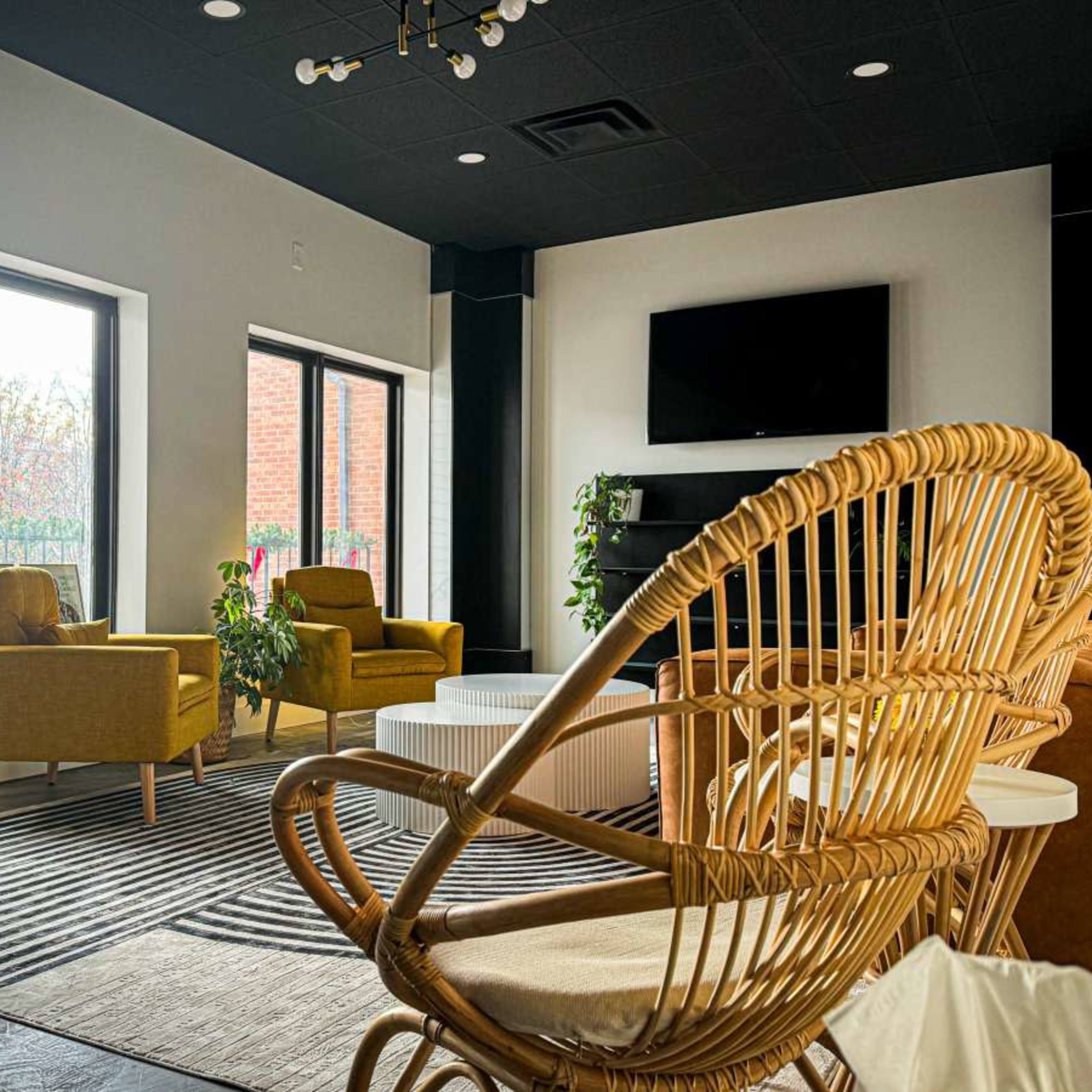 A modern, well-lit lounge area with two yellow chairs, a round white coffee table, and large windows overlooking greenery.