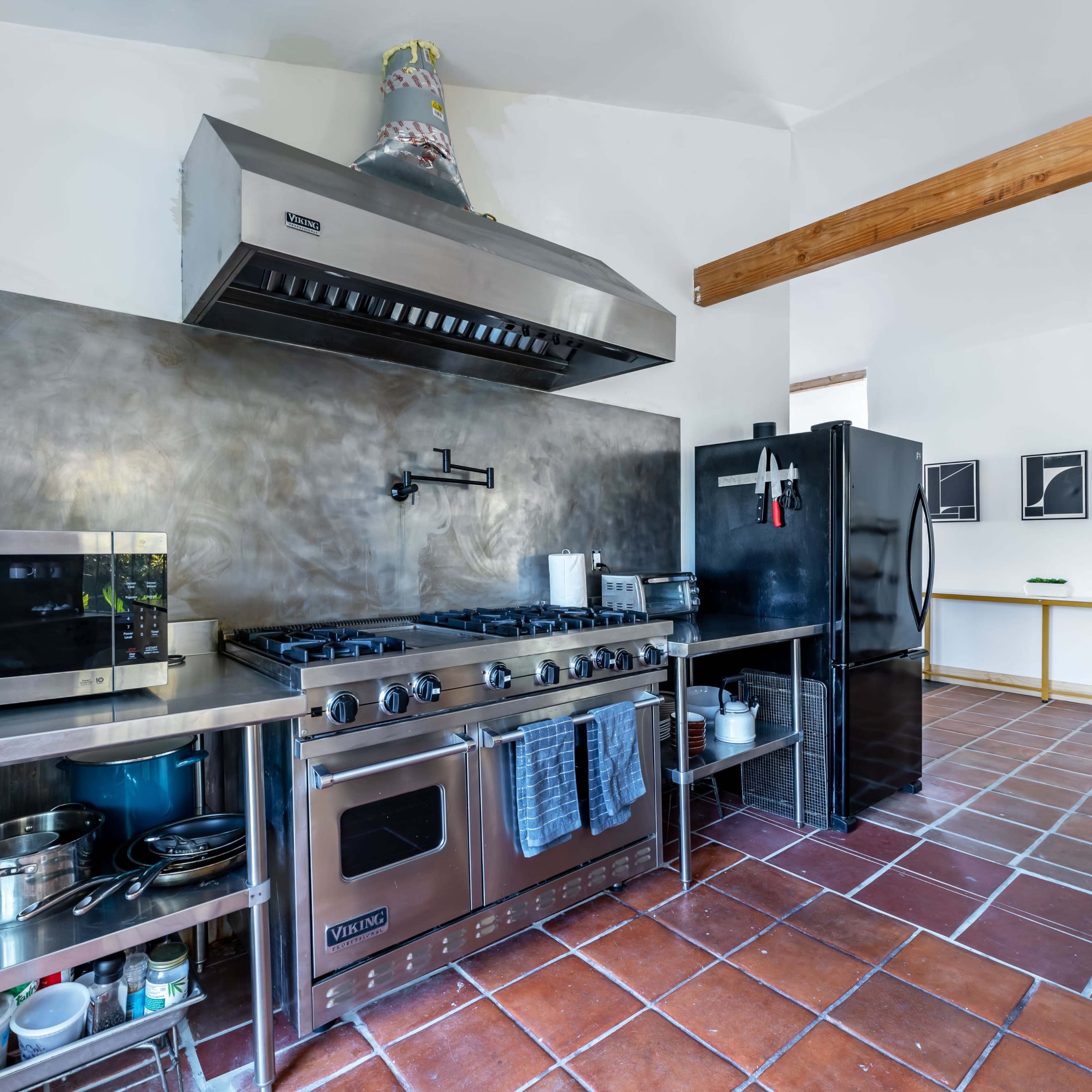 The kitchen features stainless steel appliances, a large gas stove with an overhead hood, and a tiled floor.