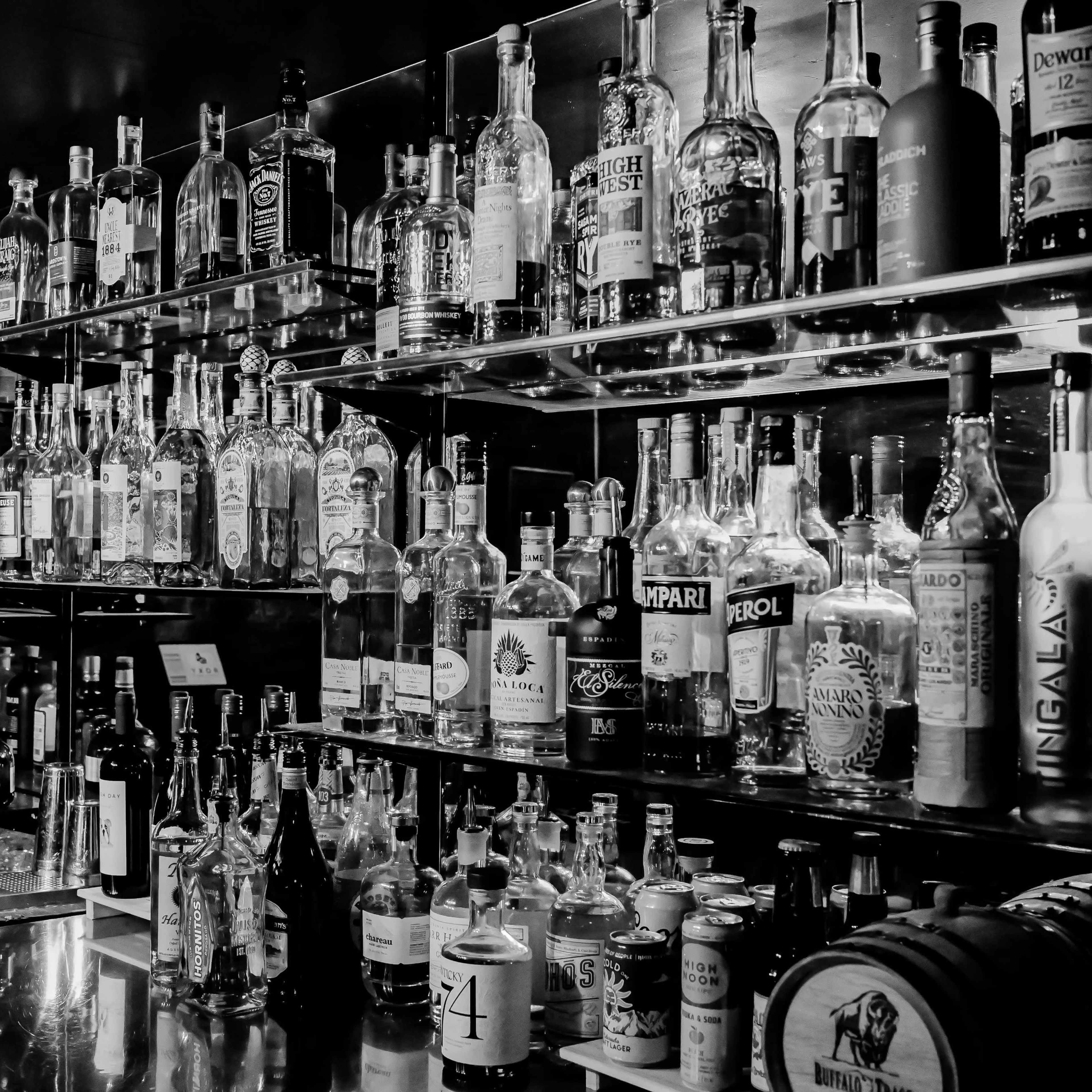 A bar shelf lined with various bottles of spirits in a black and white setting.