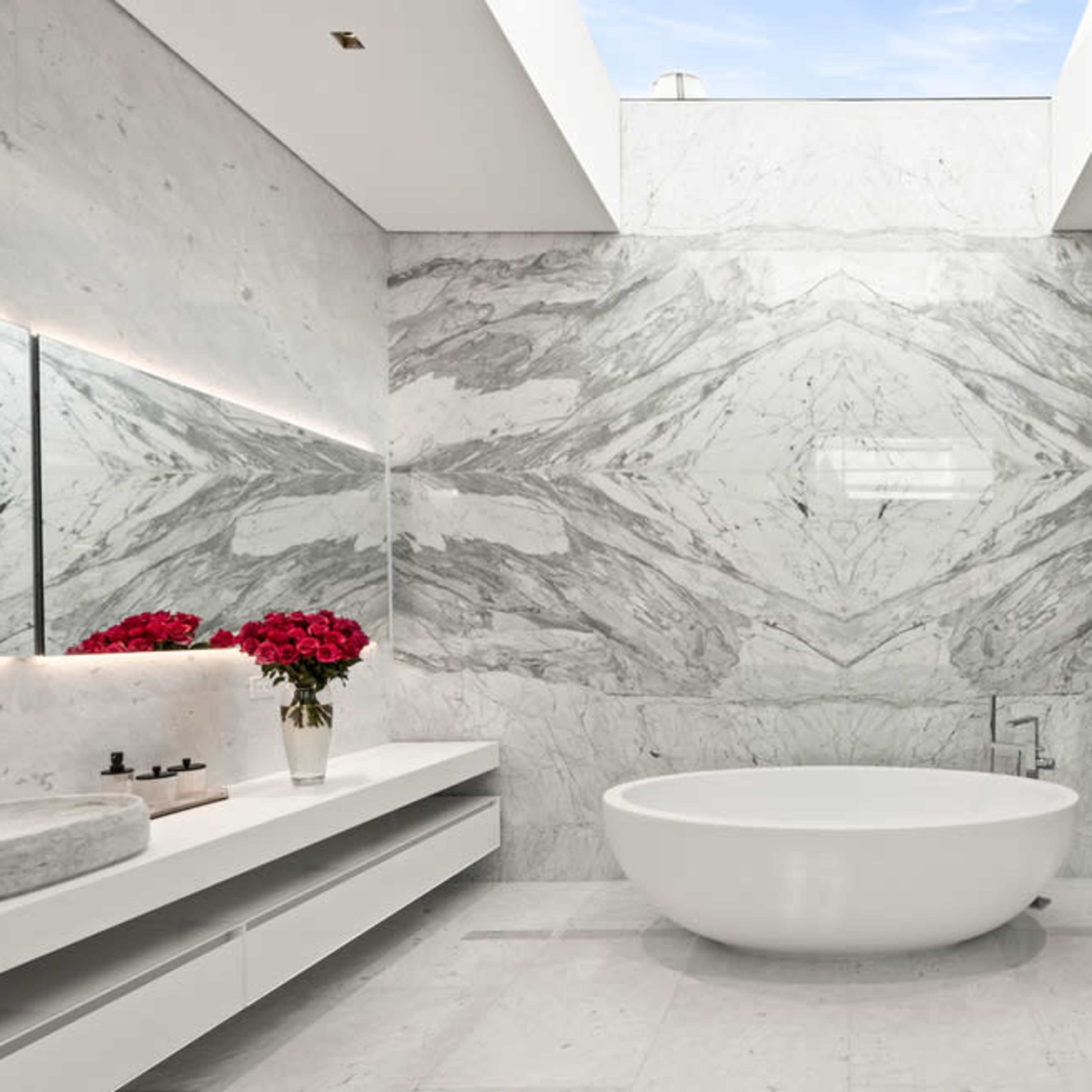 The bathroom features a large freestanding bathtub, a minimalist vanity with a stone sink, and a marble accent wall adorned with flowers.