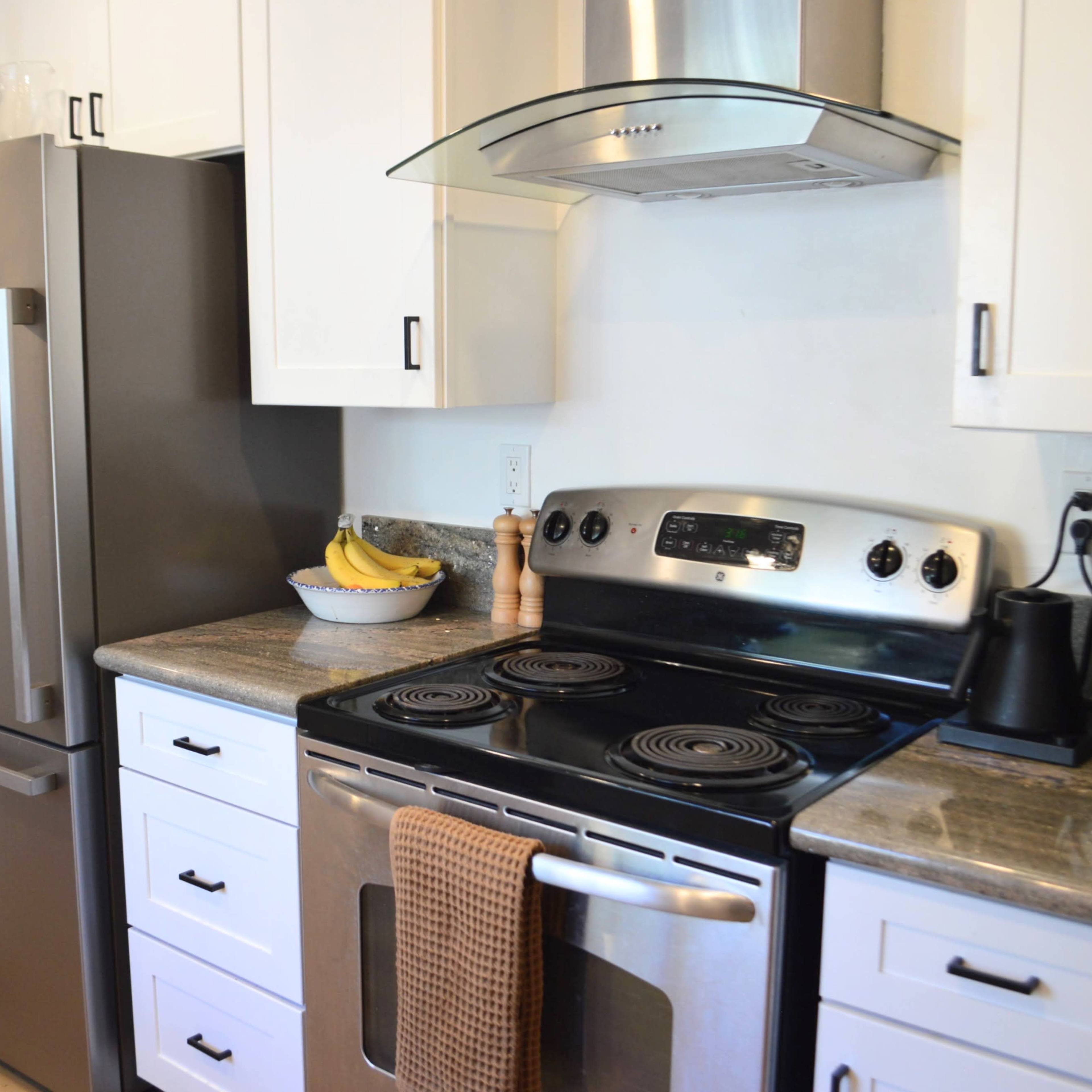 A modern kitchen with stainless steel appliances, including a refrigerator and an oven, along with a granite countertop and white cabinetry.