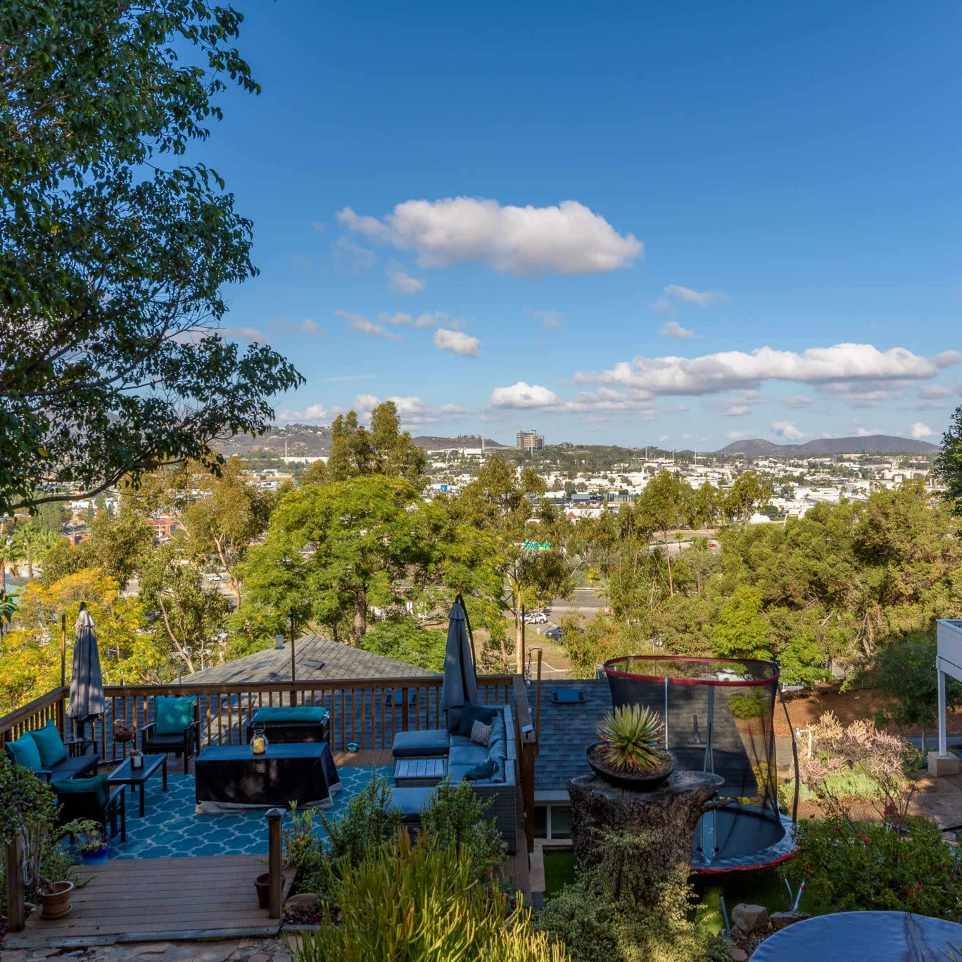 A hillside patio overlooking a city with trees and clouds scattered in the sky.