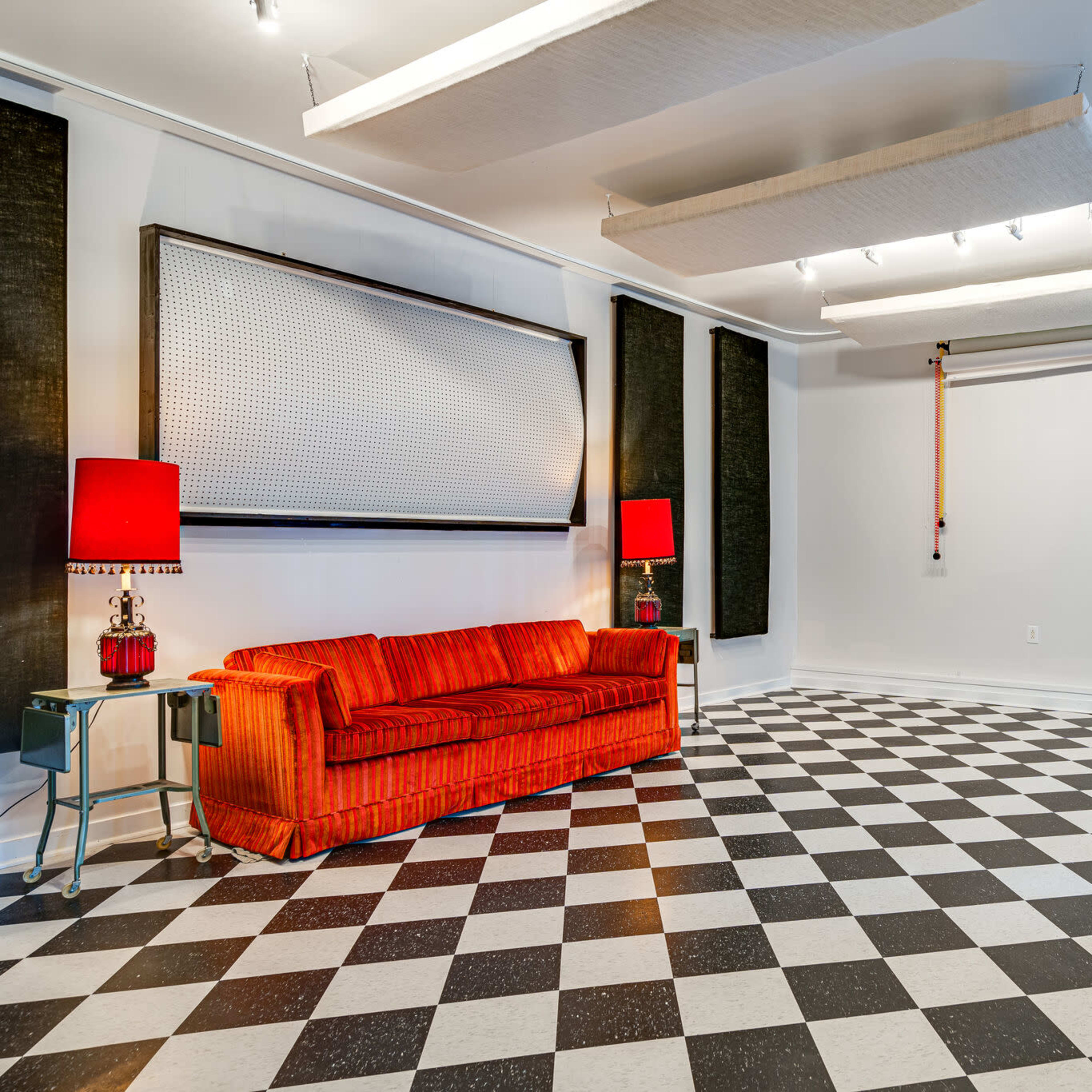 A room with a checkered black and white floor, a red couch, and two red lamps on side tables.