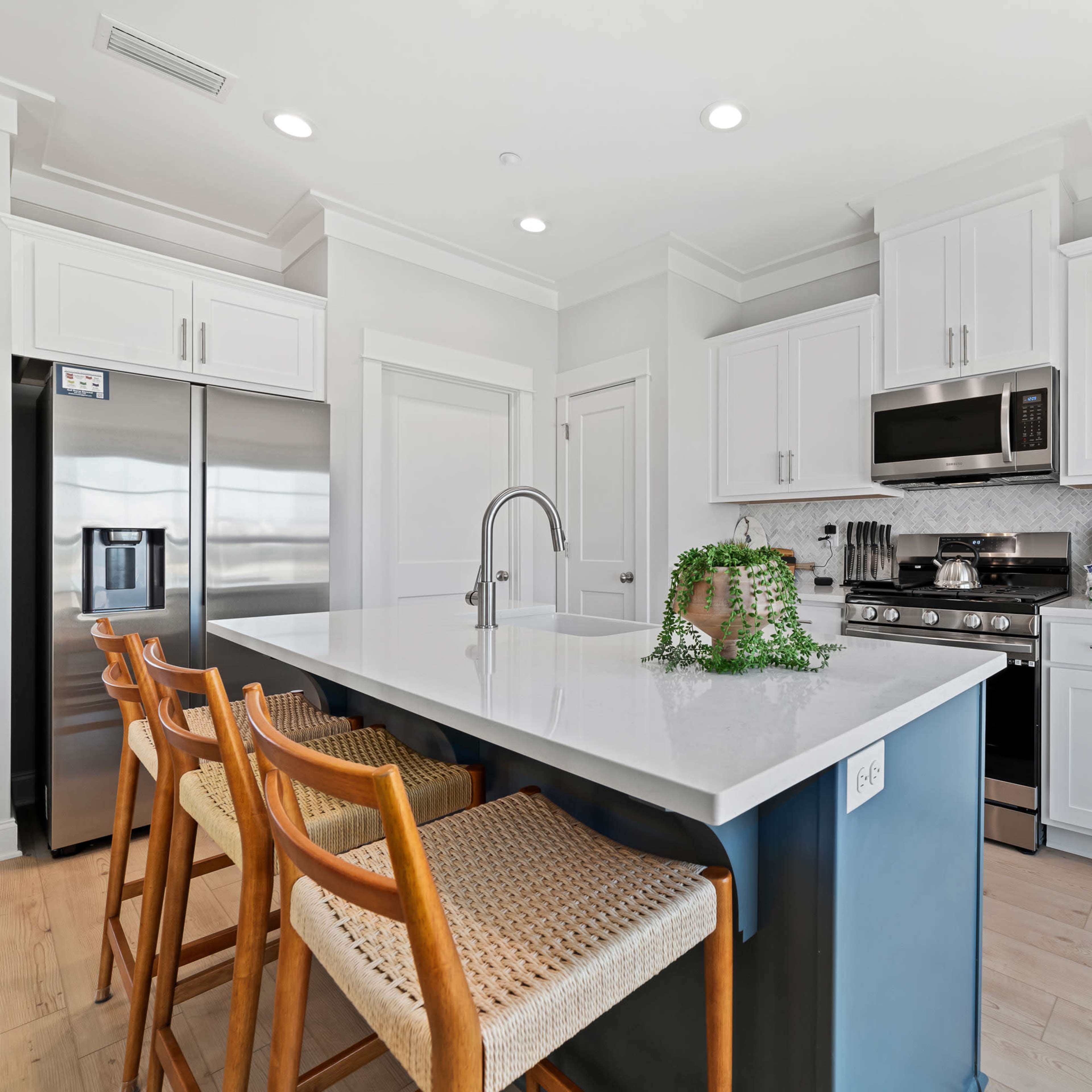 A modern kitchen features white cabinetry, stainless steel appliances, a central island with seating, and light wood flooring.