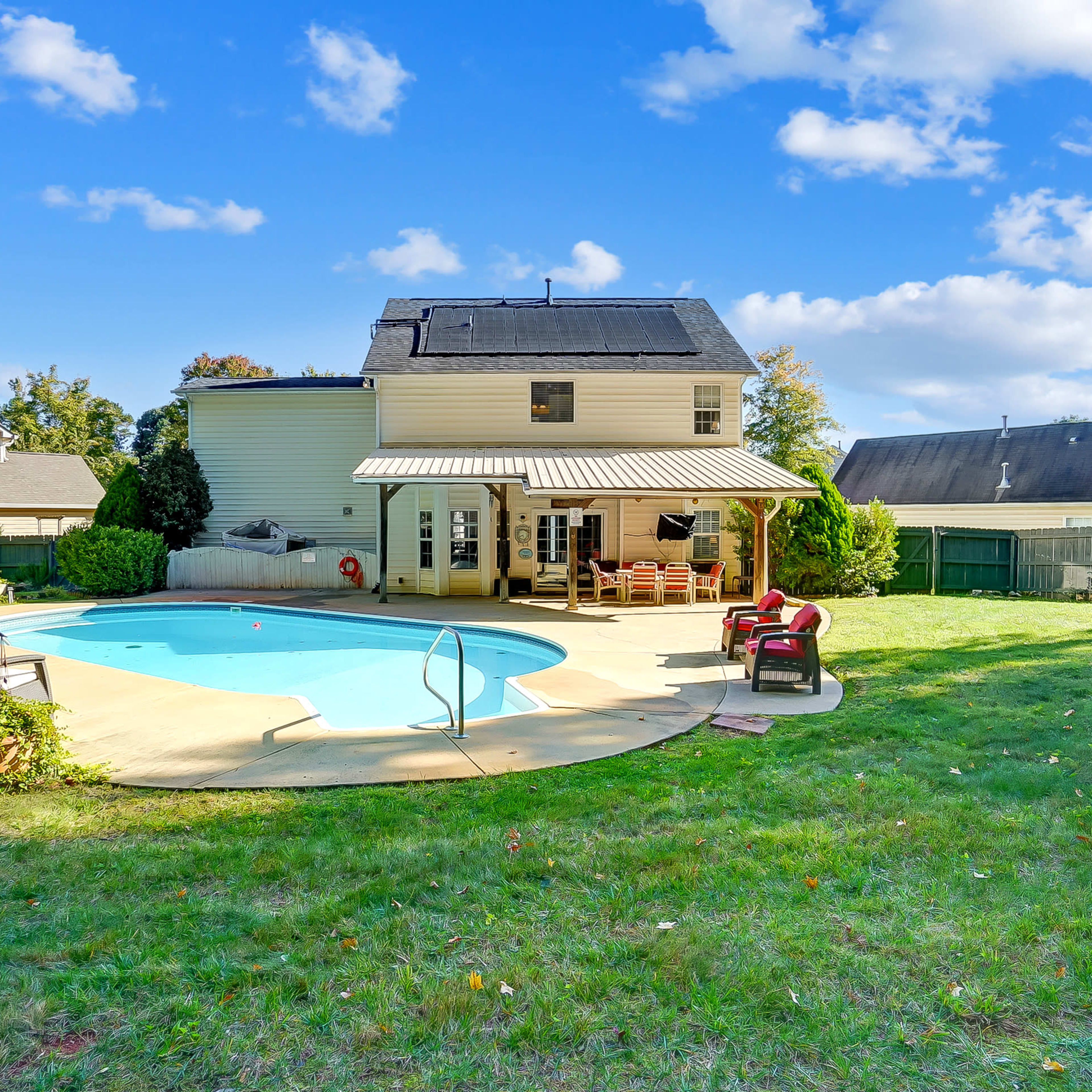 A backyard featuring a swimming pool, a two-story house, and a well-maintained lawn surrounded by a wooden fence.