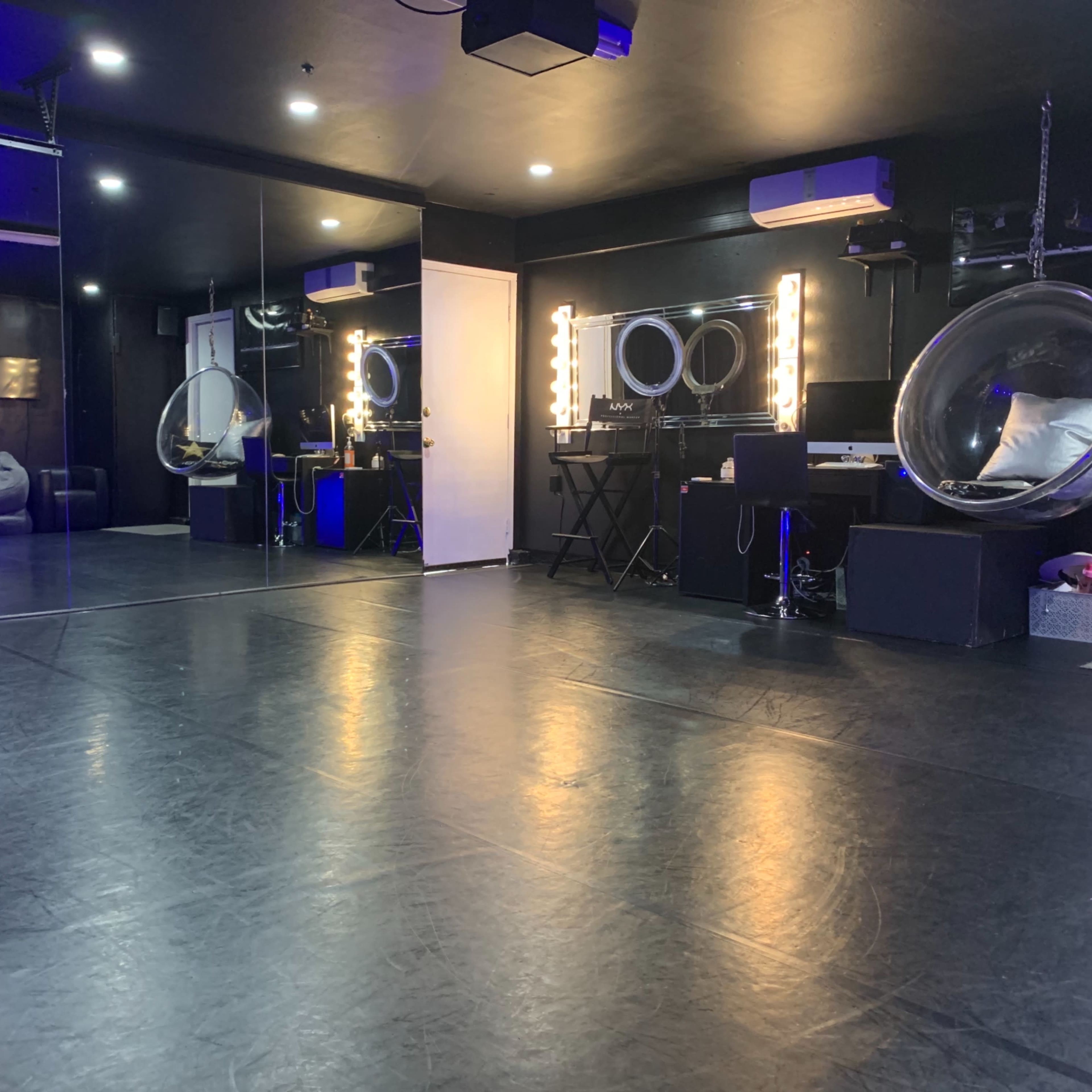 The interior of a studio features a mirrored wall, illuminated makeup stations, and a polished floor.