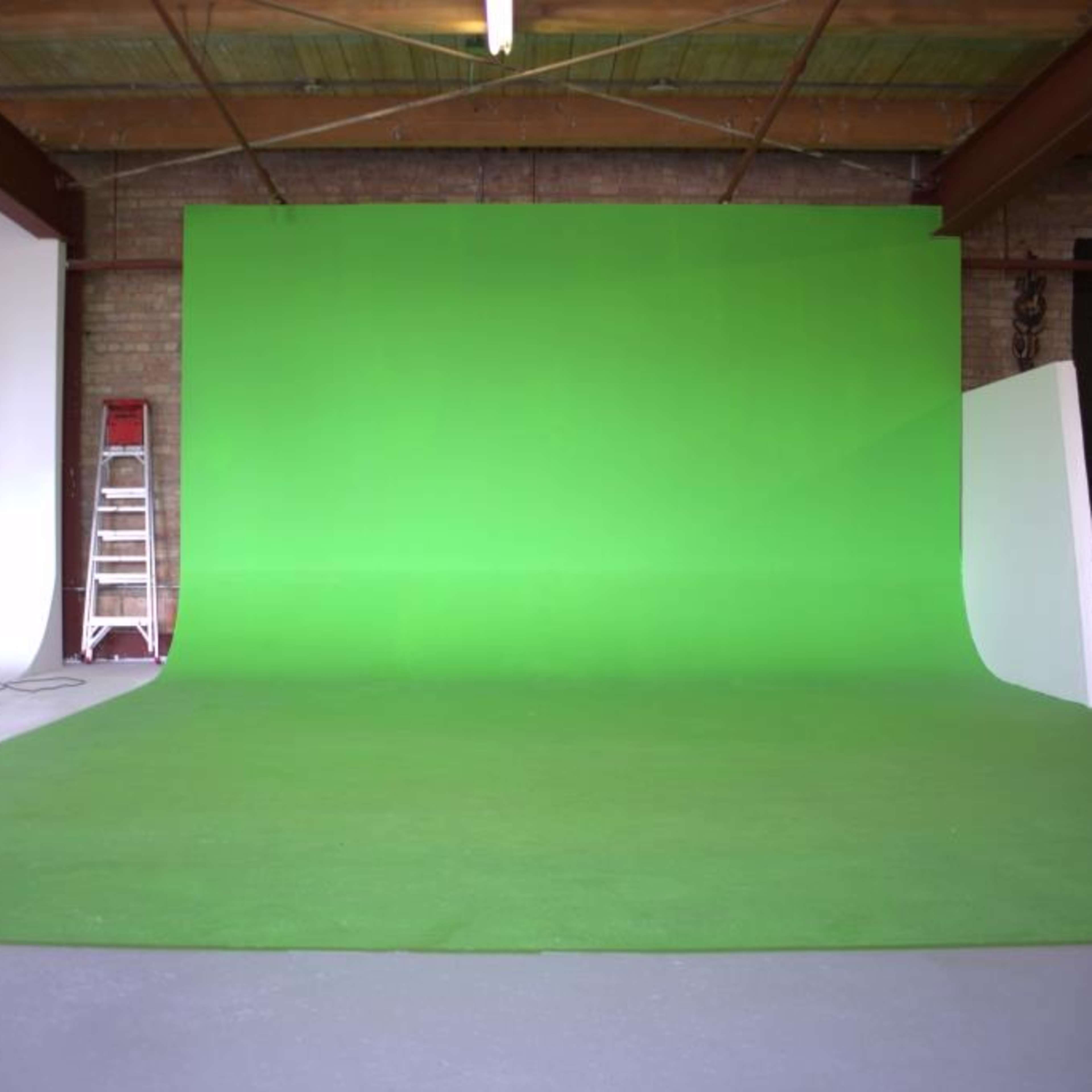 A studio space with a large green backdrop, a ladder, a microphone stand, and a black couch in the corner.