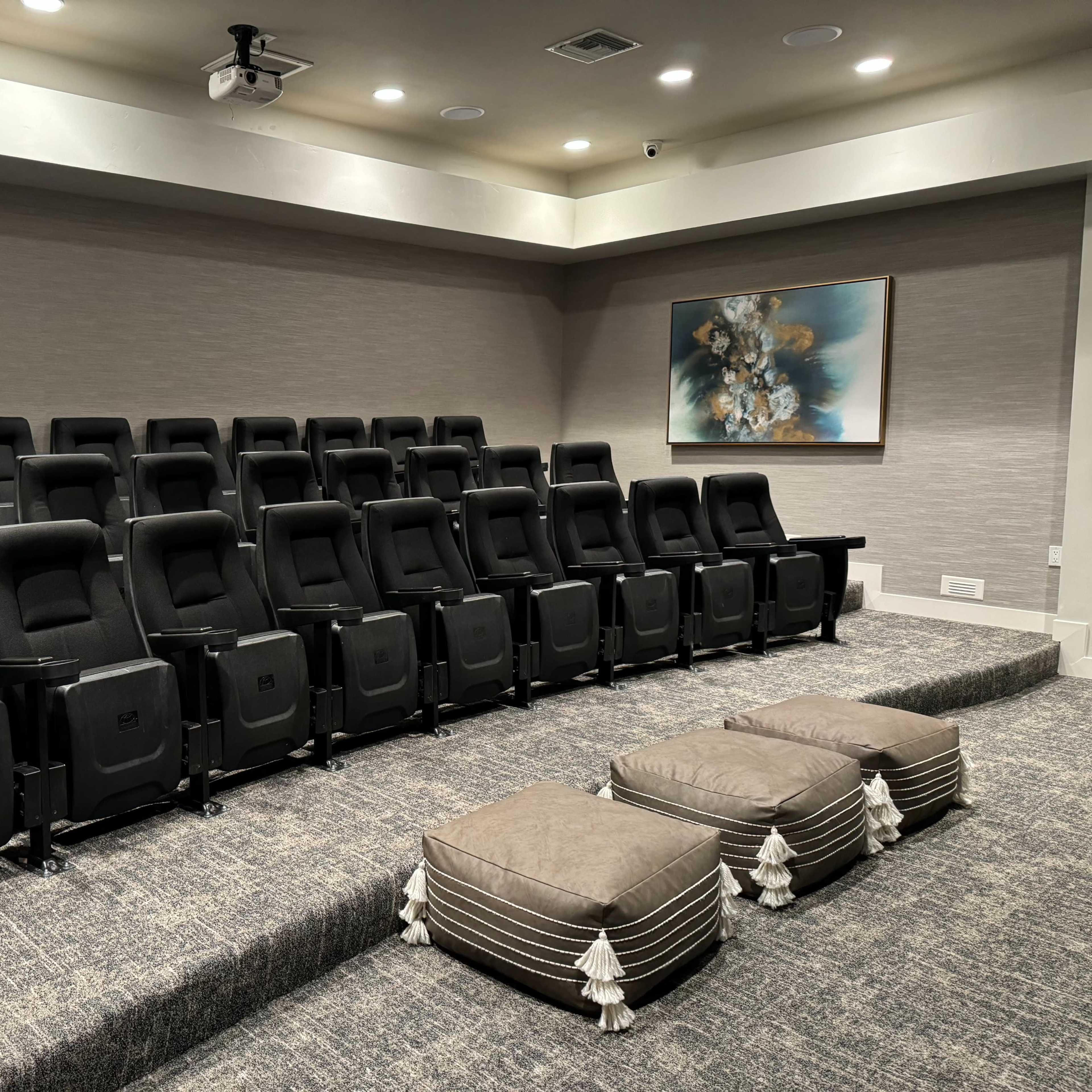 A small home theater with rows of black recliner seats and two decorative ottomans in the front.