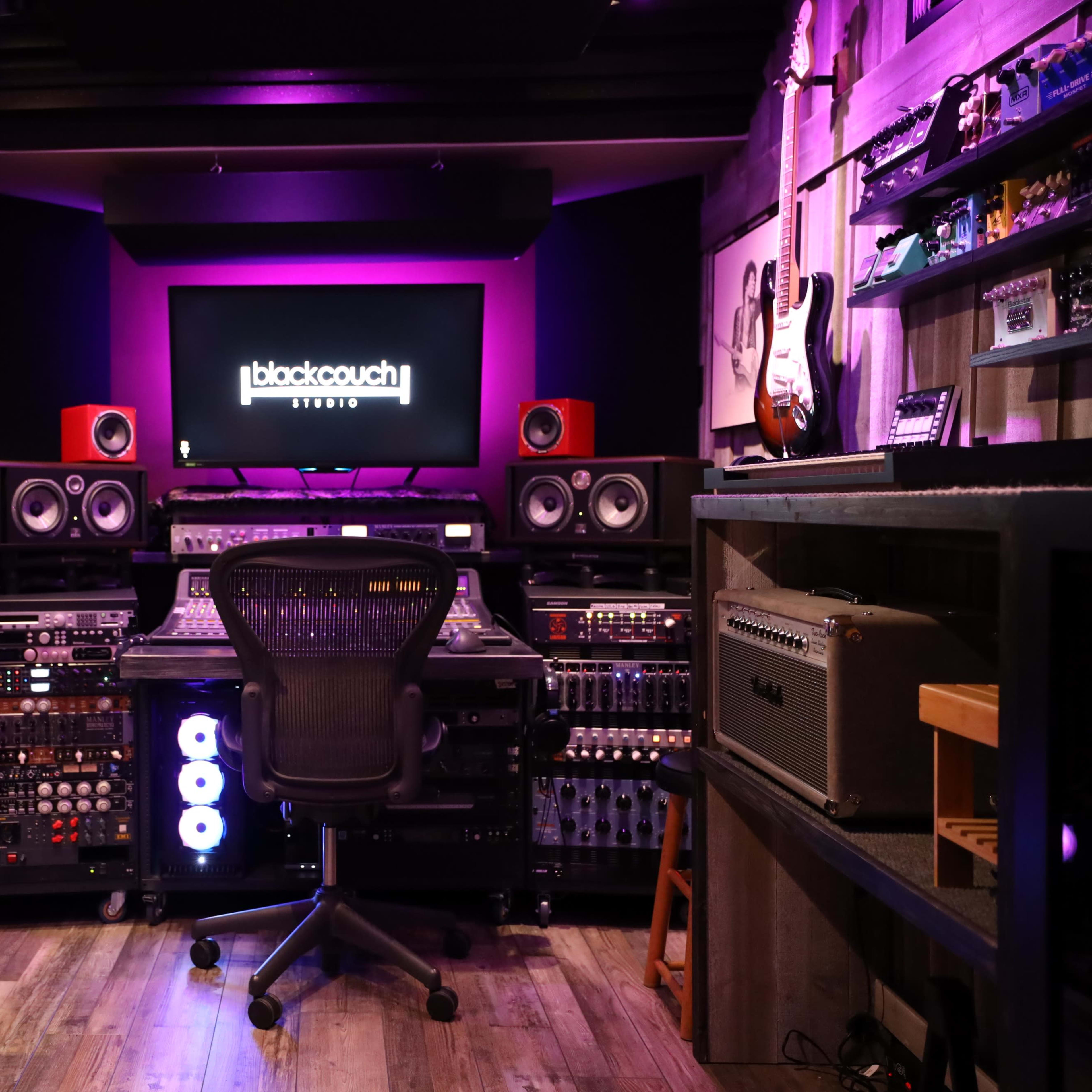 An audio recording studio featuring a control desk with various sound equipment, monitors, and colorful lighting.