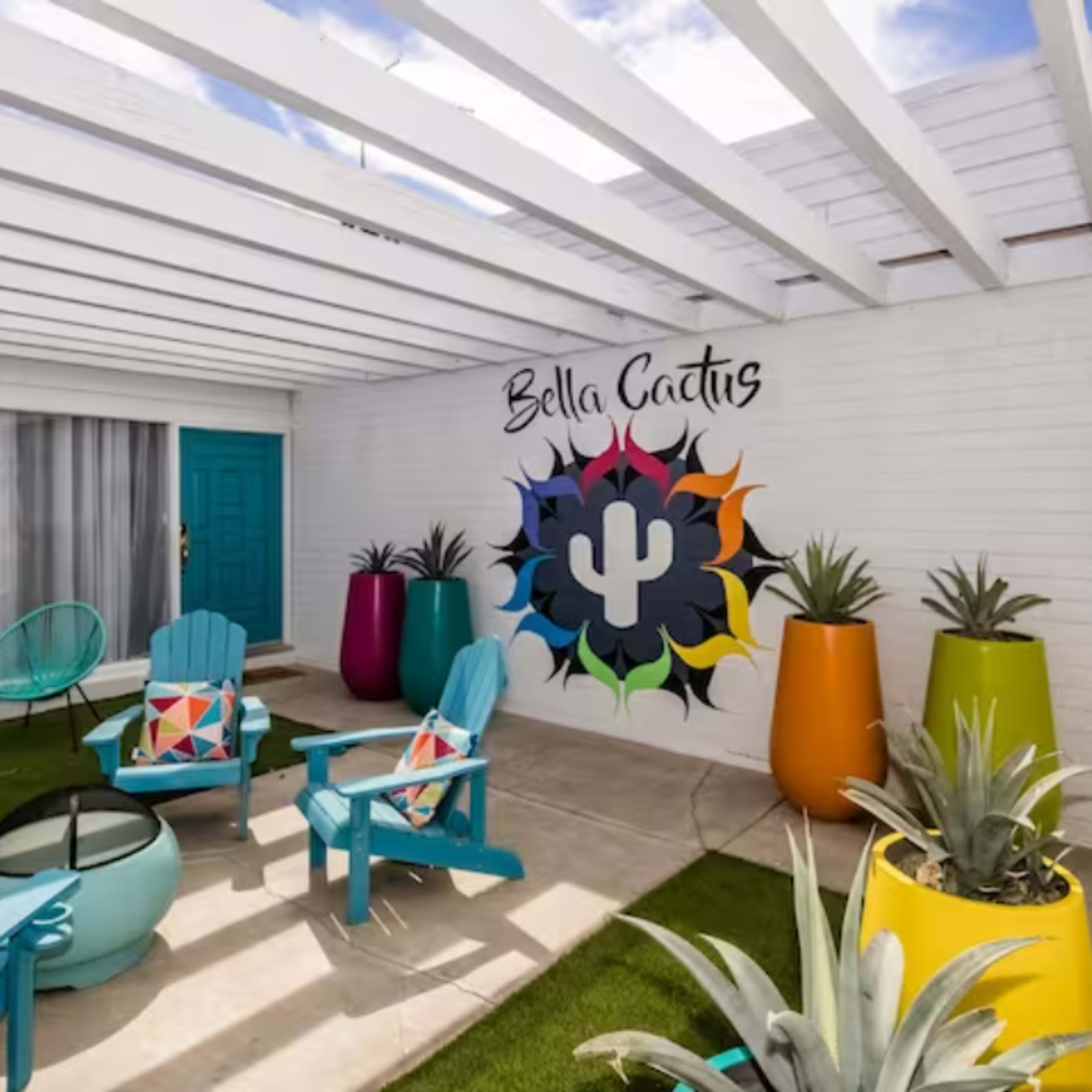 A brightly colored outdoor seating area with teal chairs and vibrant planters, featuring a decorative mural of a cactus on the wall.
