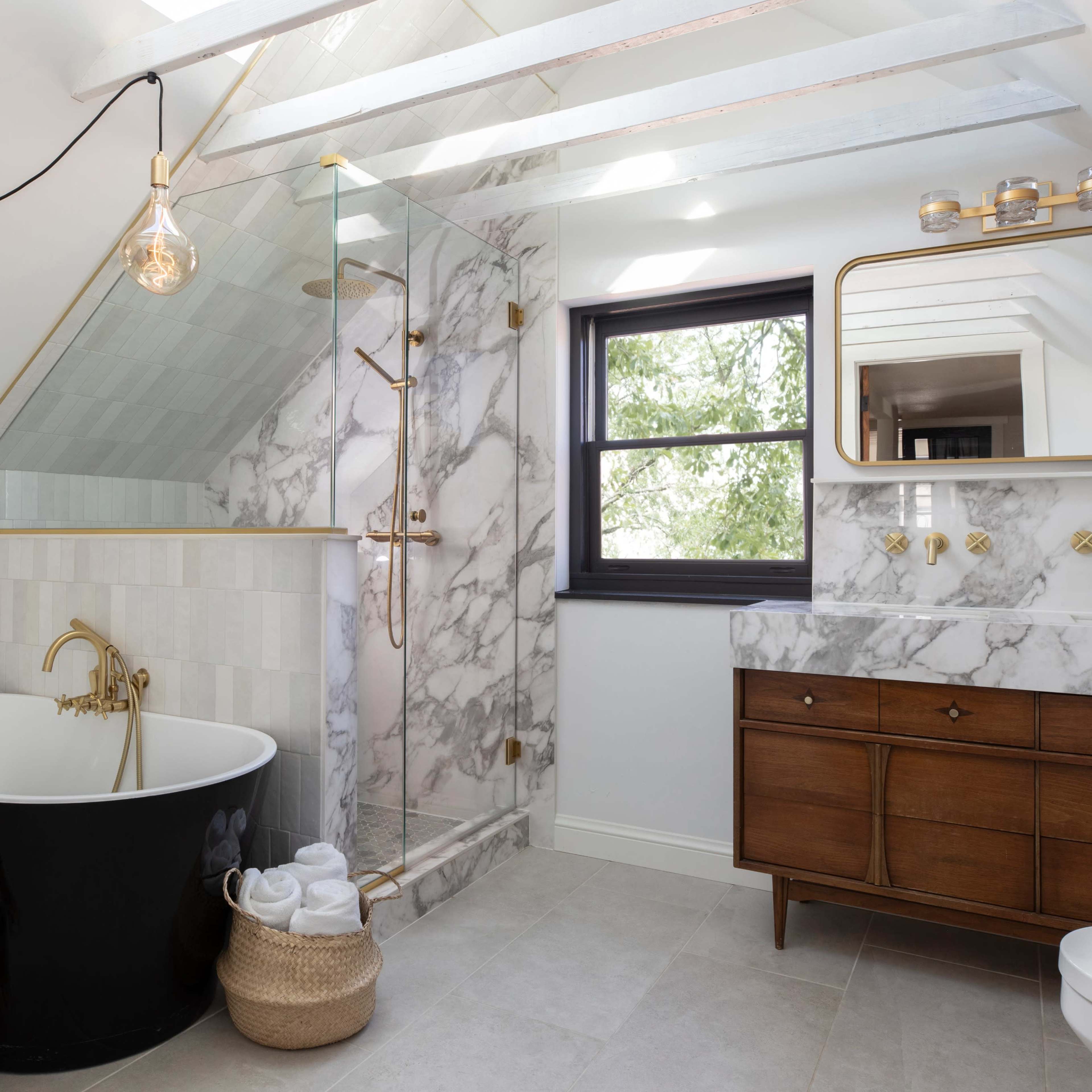 A modern bathroom featuring a freestanding black bathtub, a marble shower with gold fixtures, and a wooden vanity with a mirror.