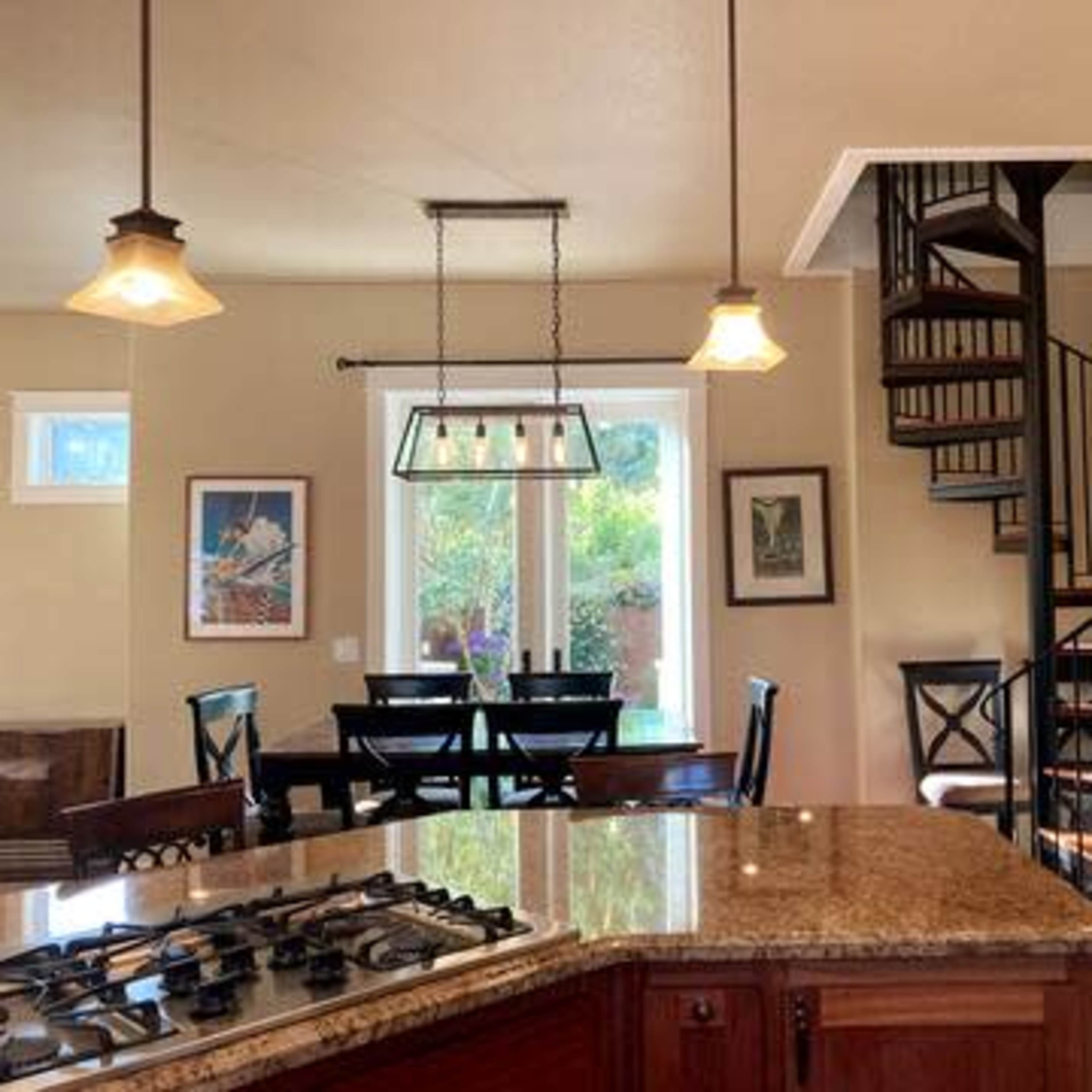 A kitchen with a large granite countertop, a spiral staircase, and a dining area with a table and chairs under pendant lighting.
