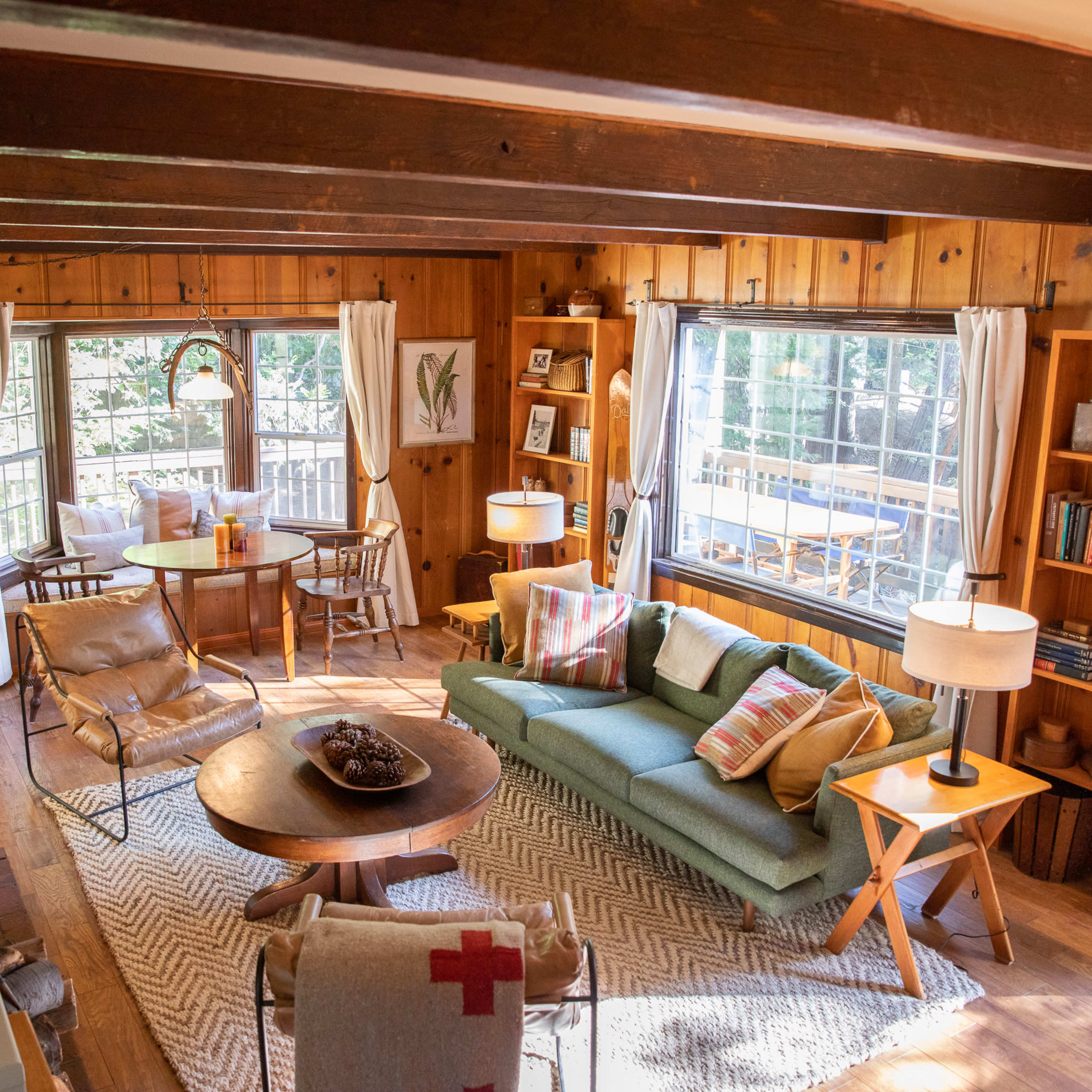 A cozy living room featuring wooden walls, a green sofa with decorative pillows, a round coffee table, and large windows providing natural light.