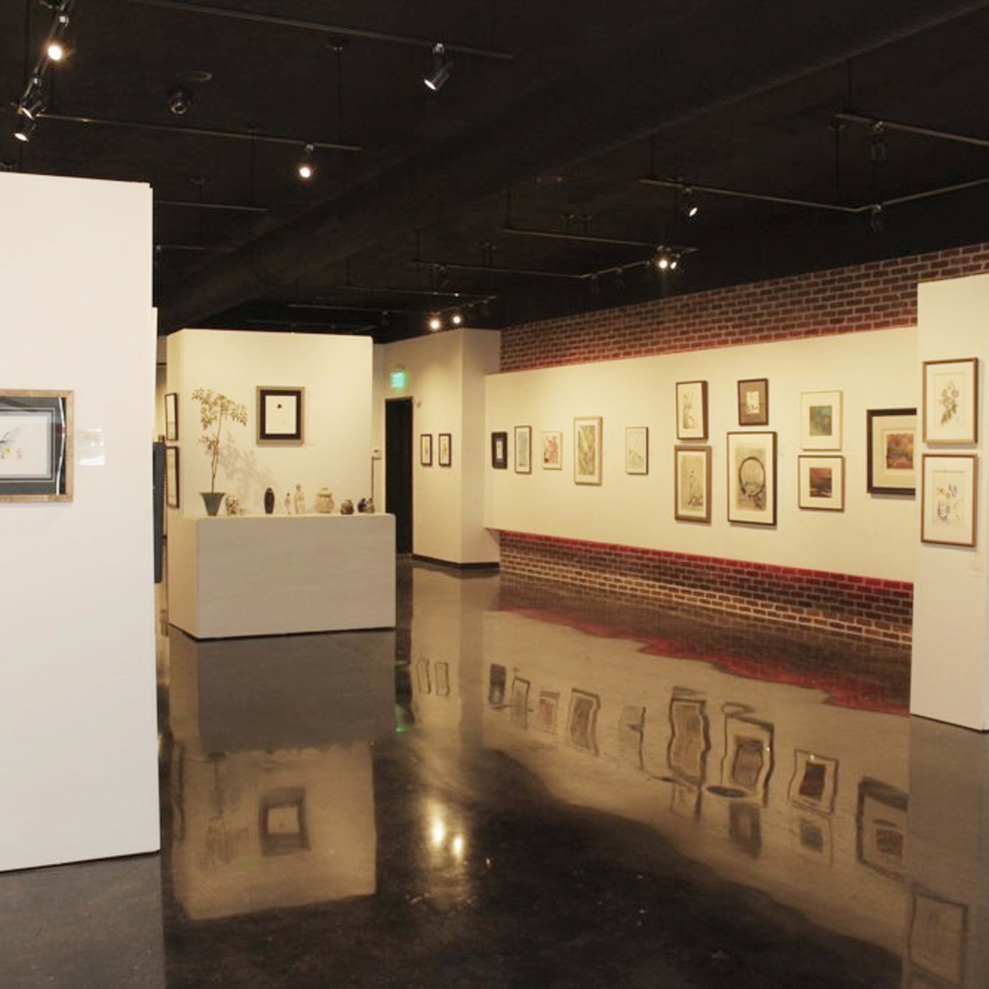 An art gallery featuring framed artwork displayed on white walls with a dark polished floor.
