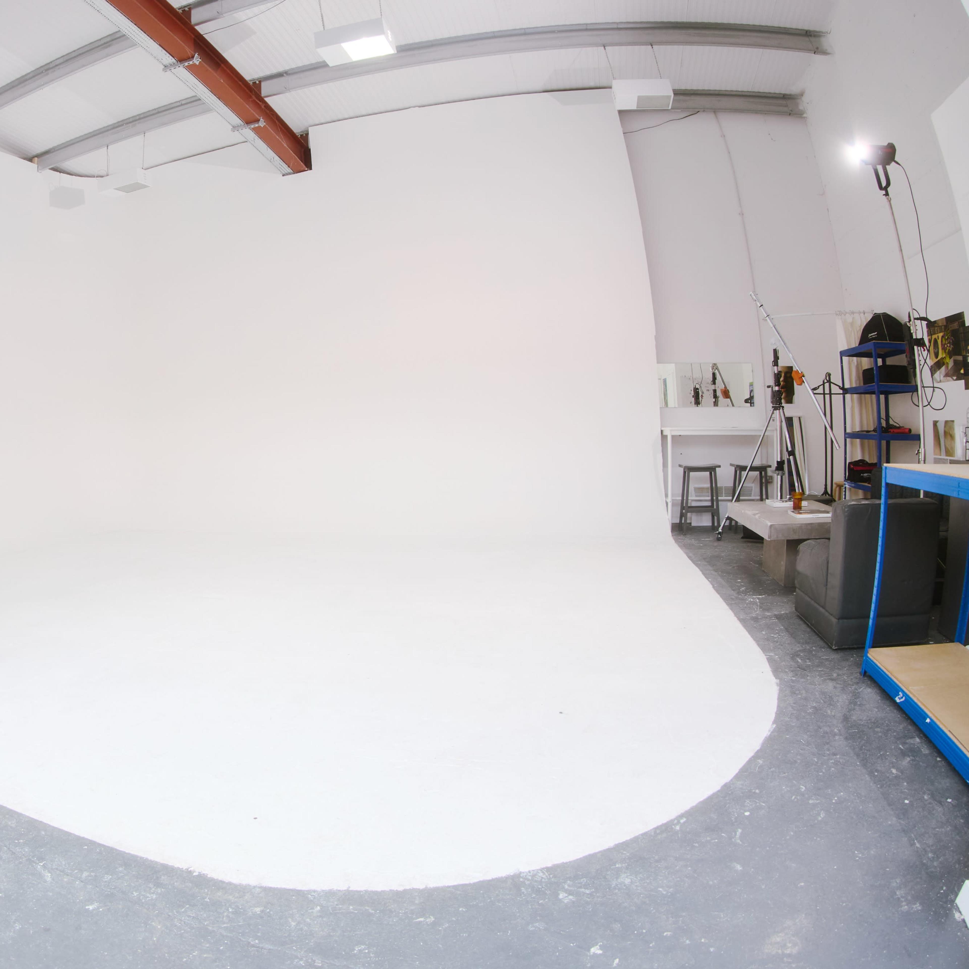 A spacious studio with white walls and a gray floor, featuring minimal equipment and a large open area.