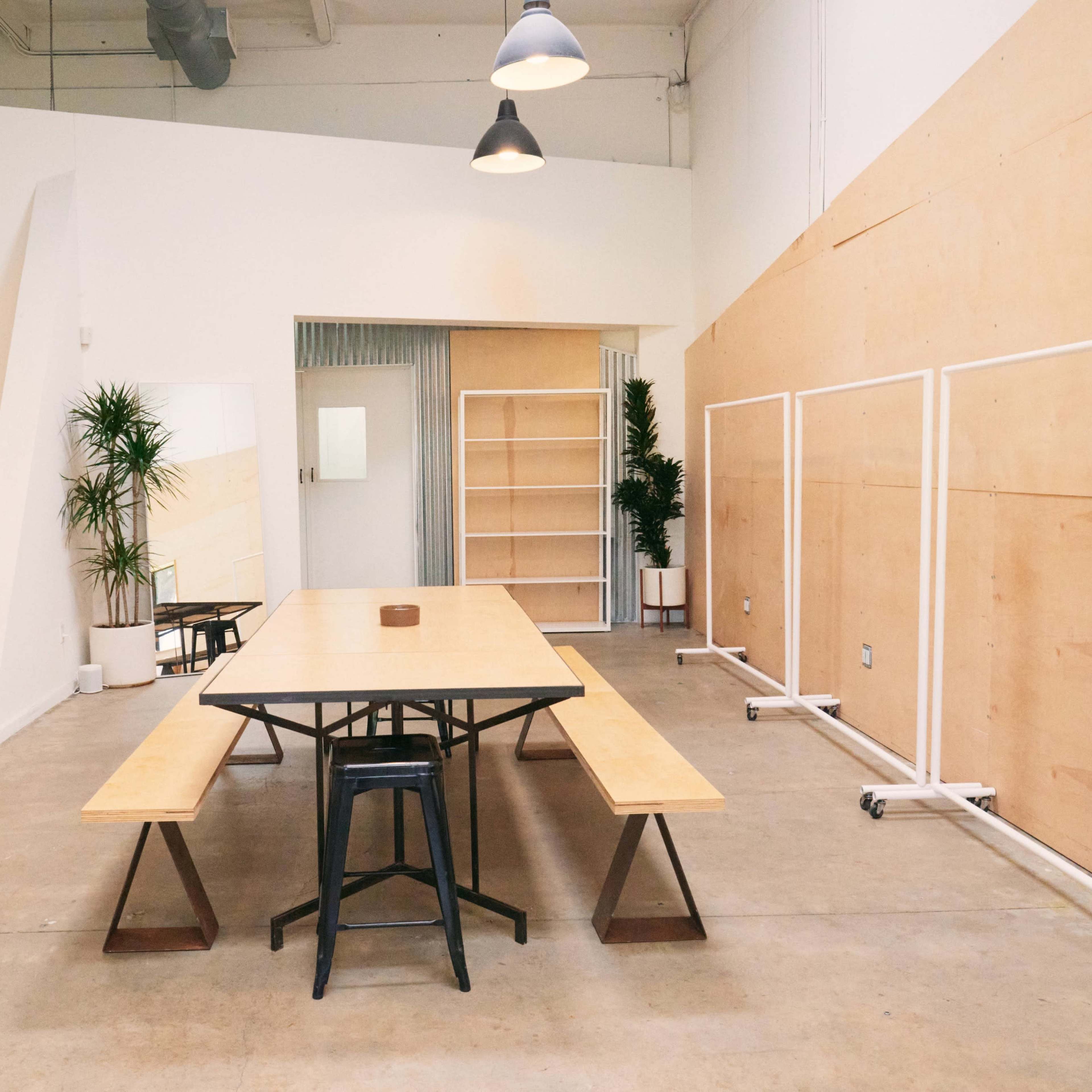 A simple meeting space features a long wooden table surrounded by benches, with minimal decor and large wooden panels along the walls.