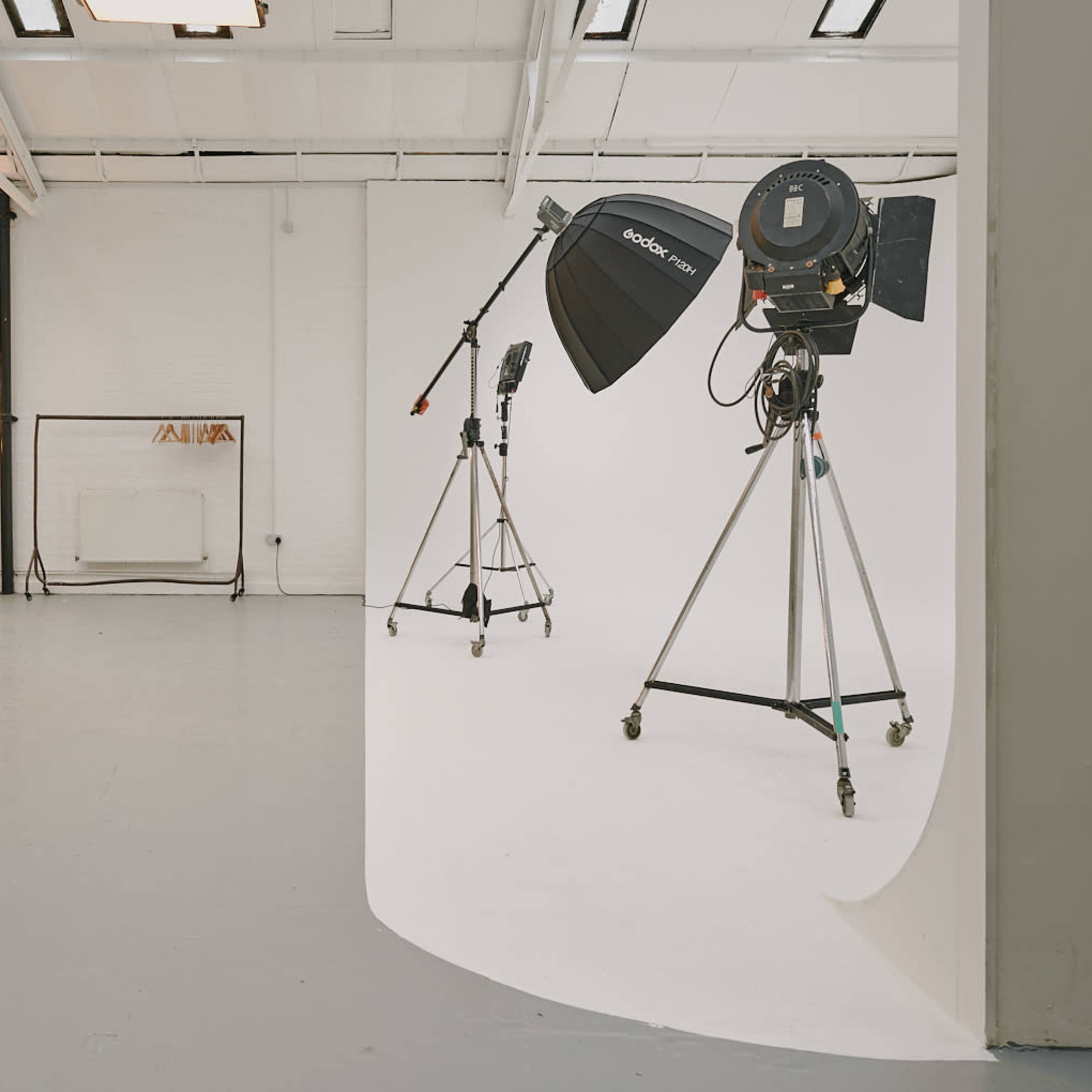 A photography studio with two light stands and a makeup station against a white backdrop.