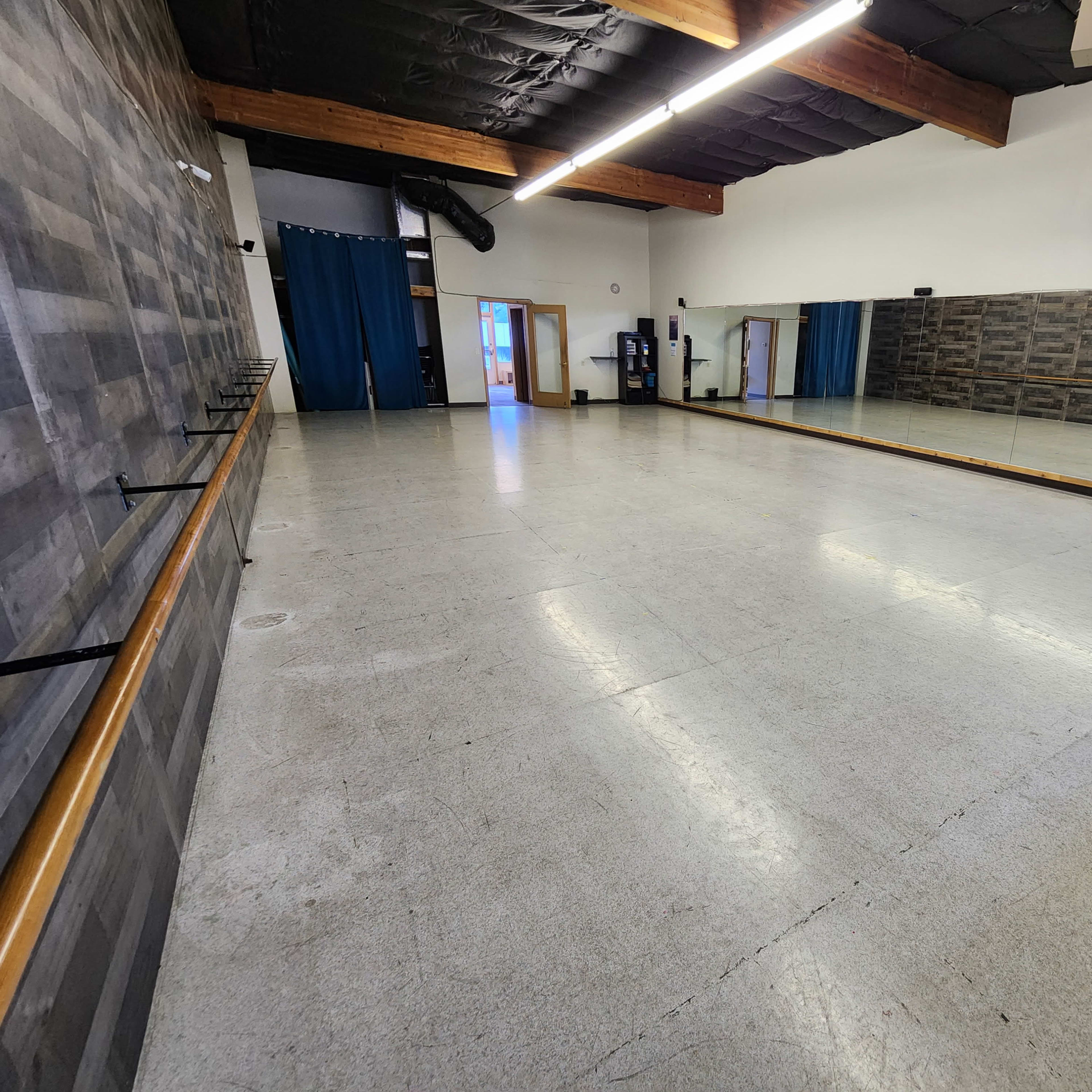 A spacious dance studio with a mirrored wall, wooden barre, and a polished floor.
