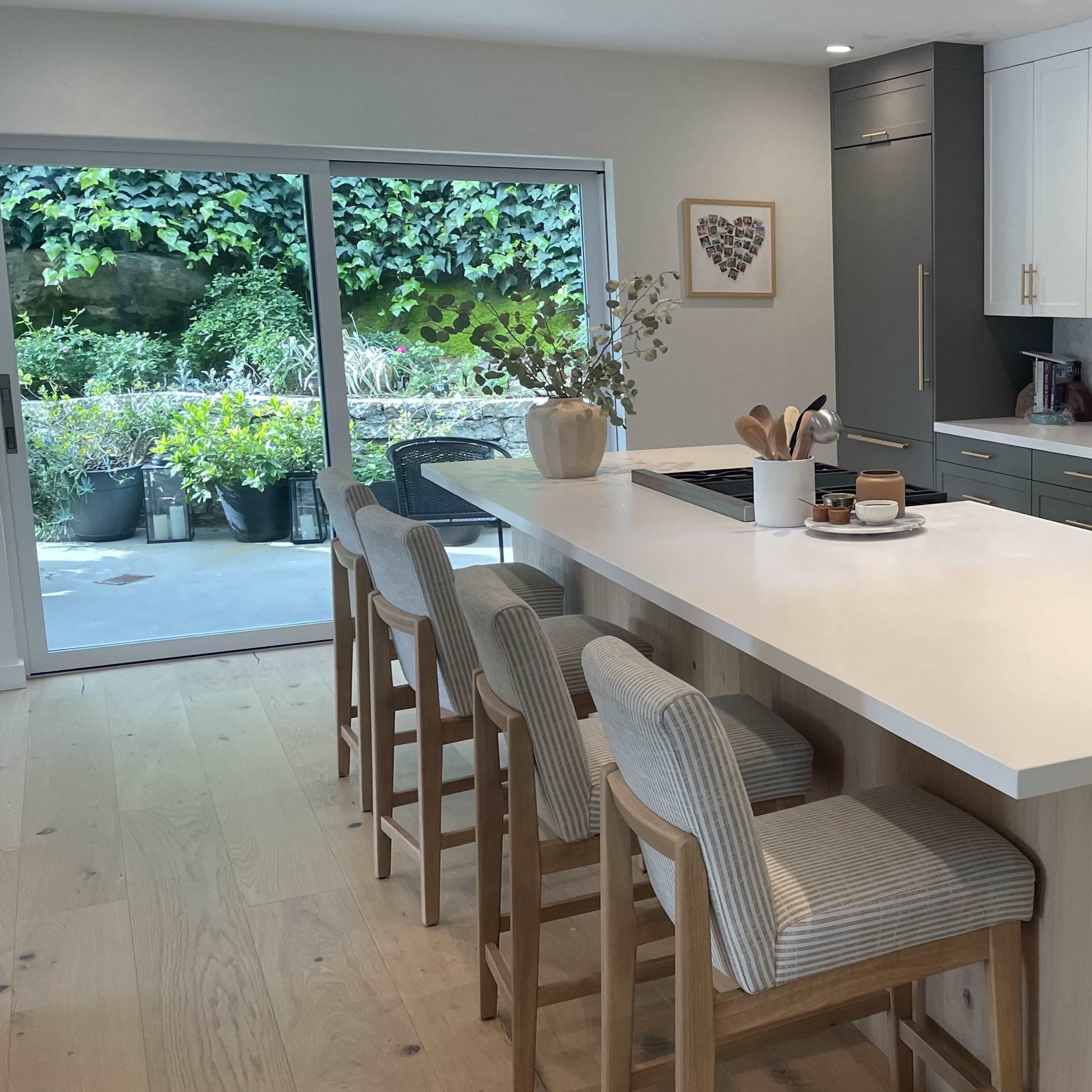 A modern kitchen features a large island with seating and opens to a garden through sliding glass doors.