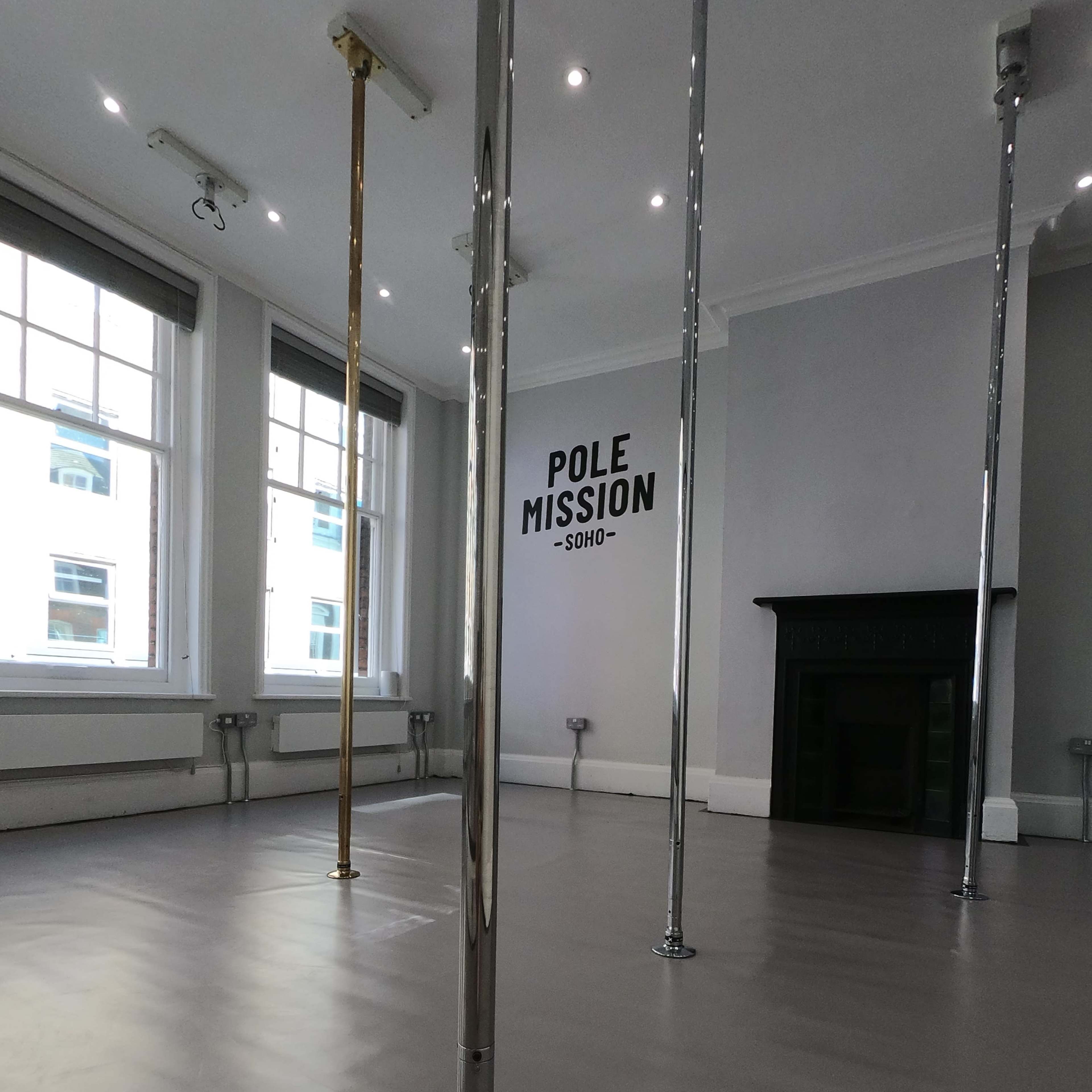 A spacious studio with multiple chrome poles, a smooth floor, and a wall featuring the text "POLE MISSION - SOHO."