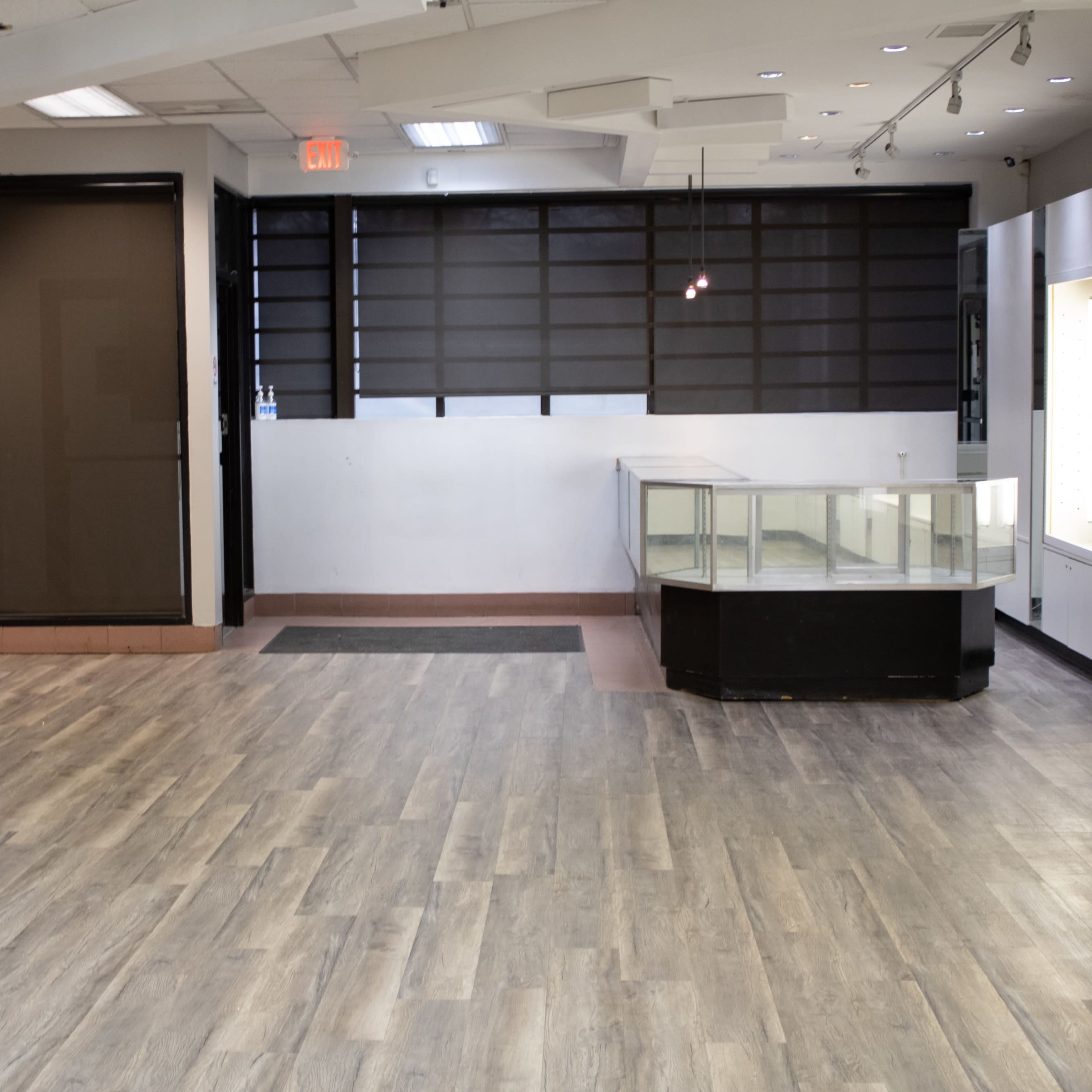An empty retail space with a wooden floor, a glass display case in the center, and a partitioned area on one side.