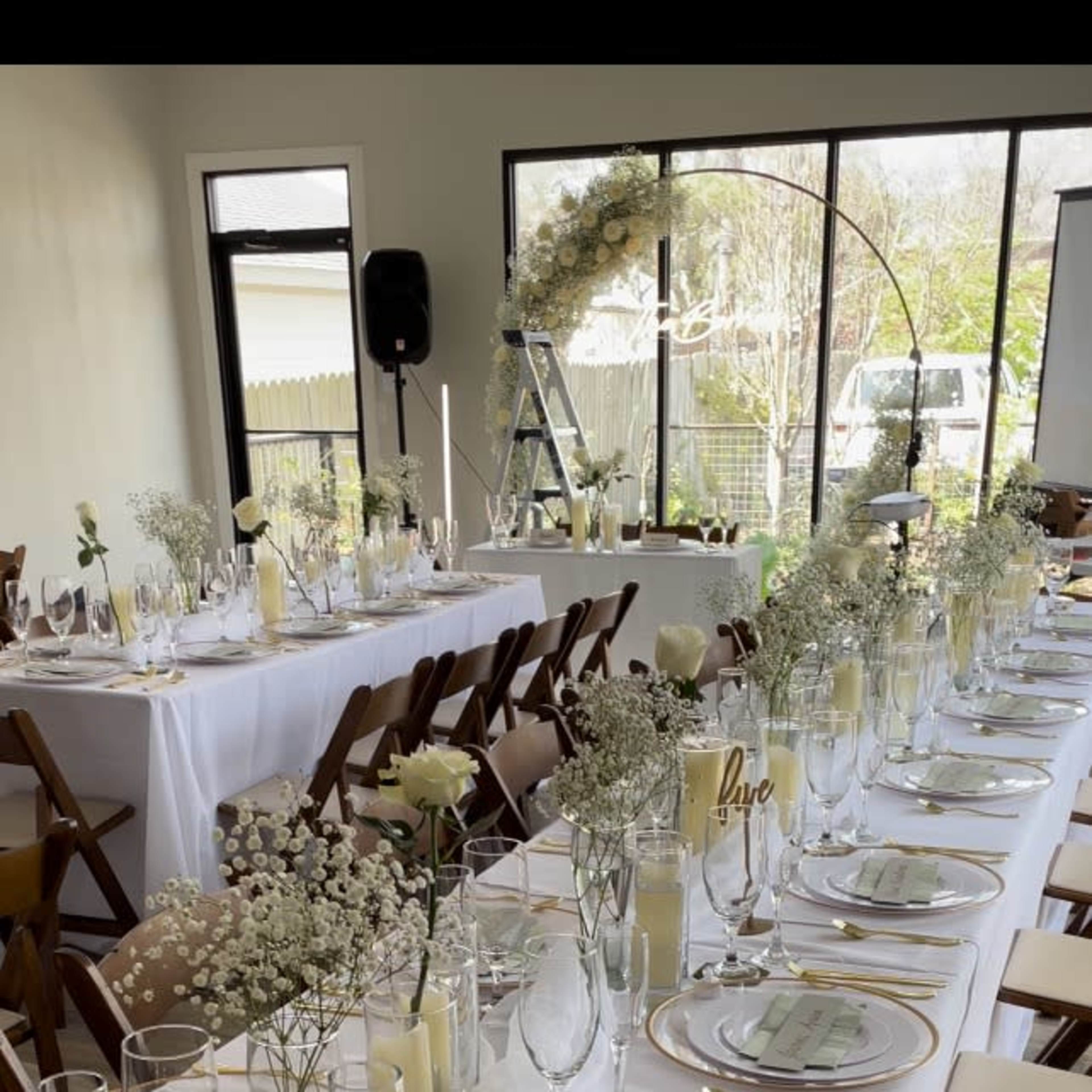 A long banquet table is set with elegant place settings, floral centerpieces, and candles, all arranged in a well-lit event space.