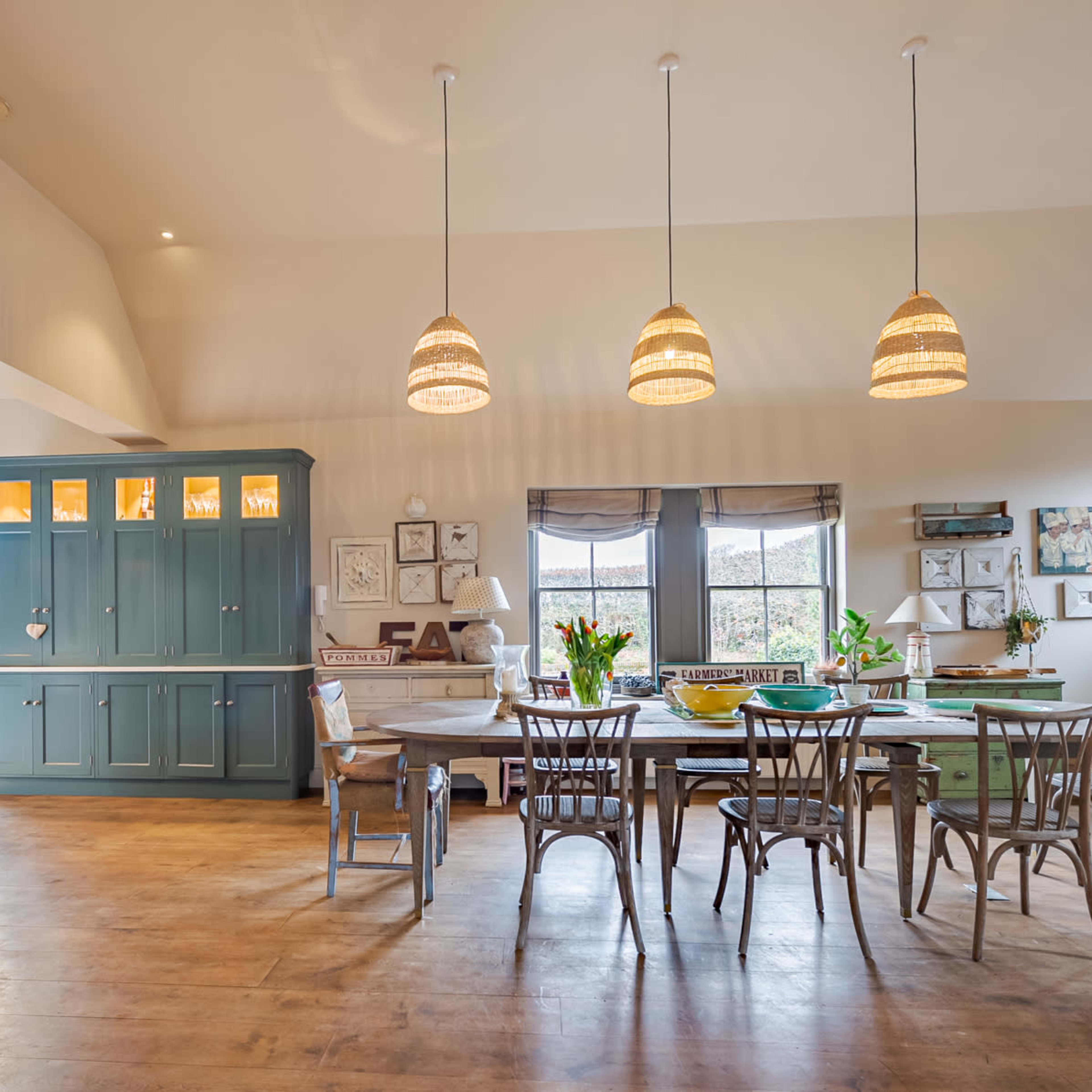 A spacious kitchen and dining area featuring a large table surrounded by chairs, a green cabinet, and pendant lights hanging from the ceiling.
