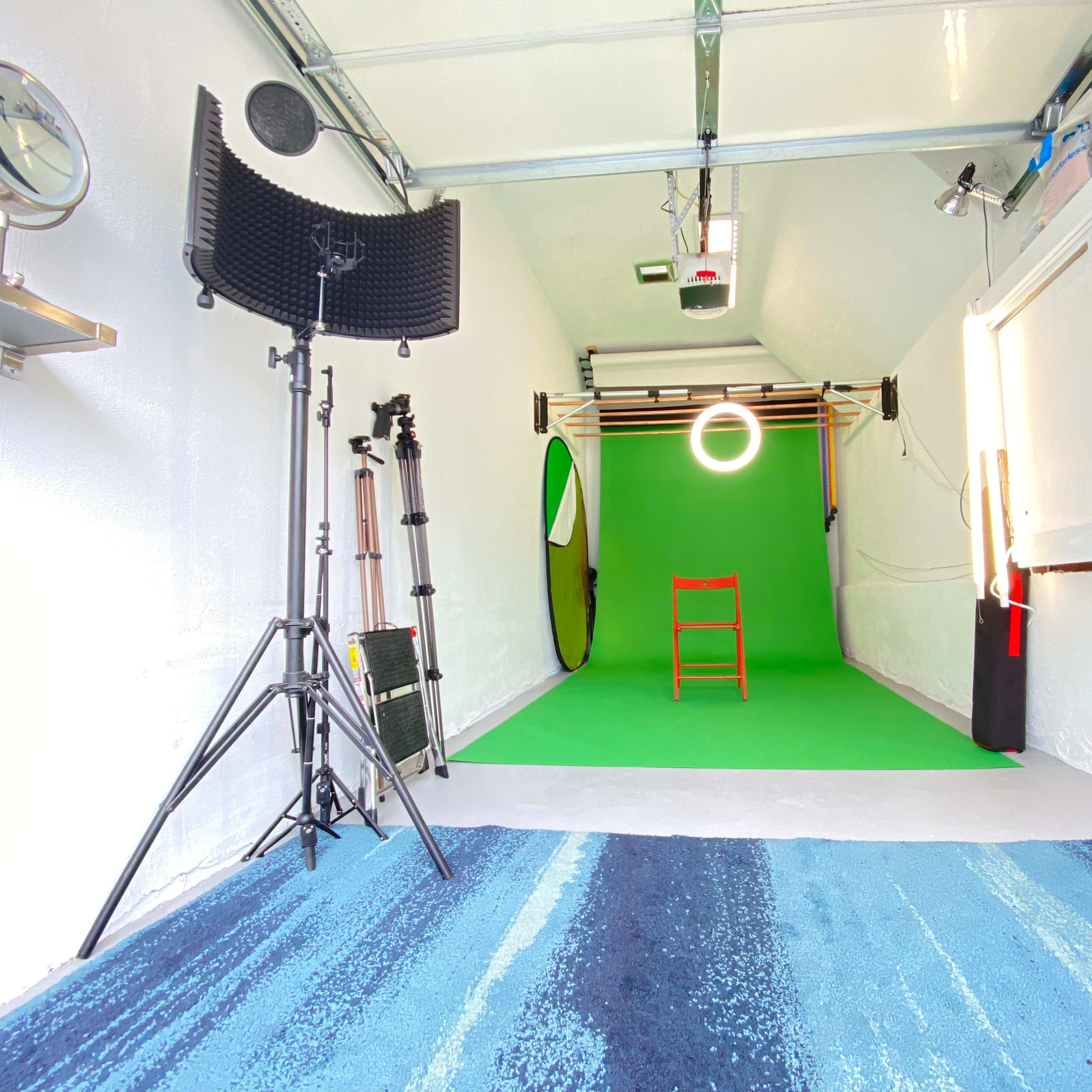 A studio space with a green backdrop, a red chair positioned in front, various lighting equipment, and a striped blue rug on the floor.
