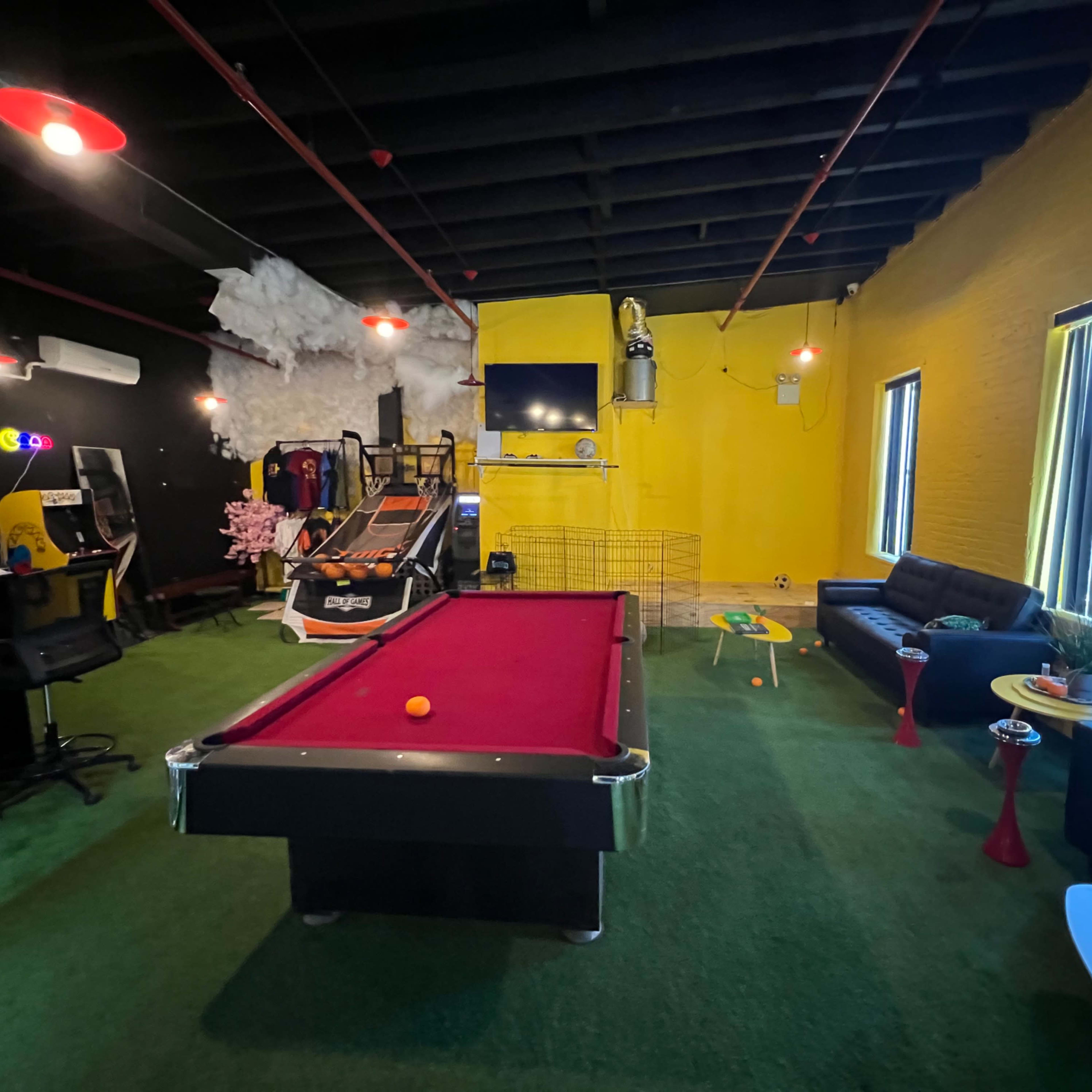 A recreational room featuring a pool table, arcade games, a turf floor, and a seating area with sofas and a coffee table.
