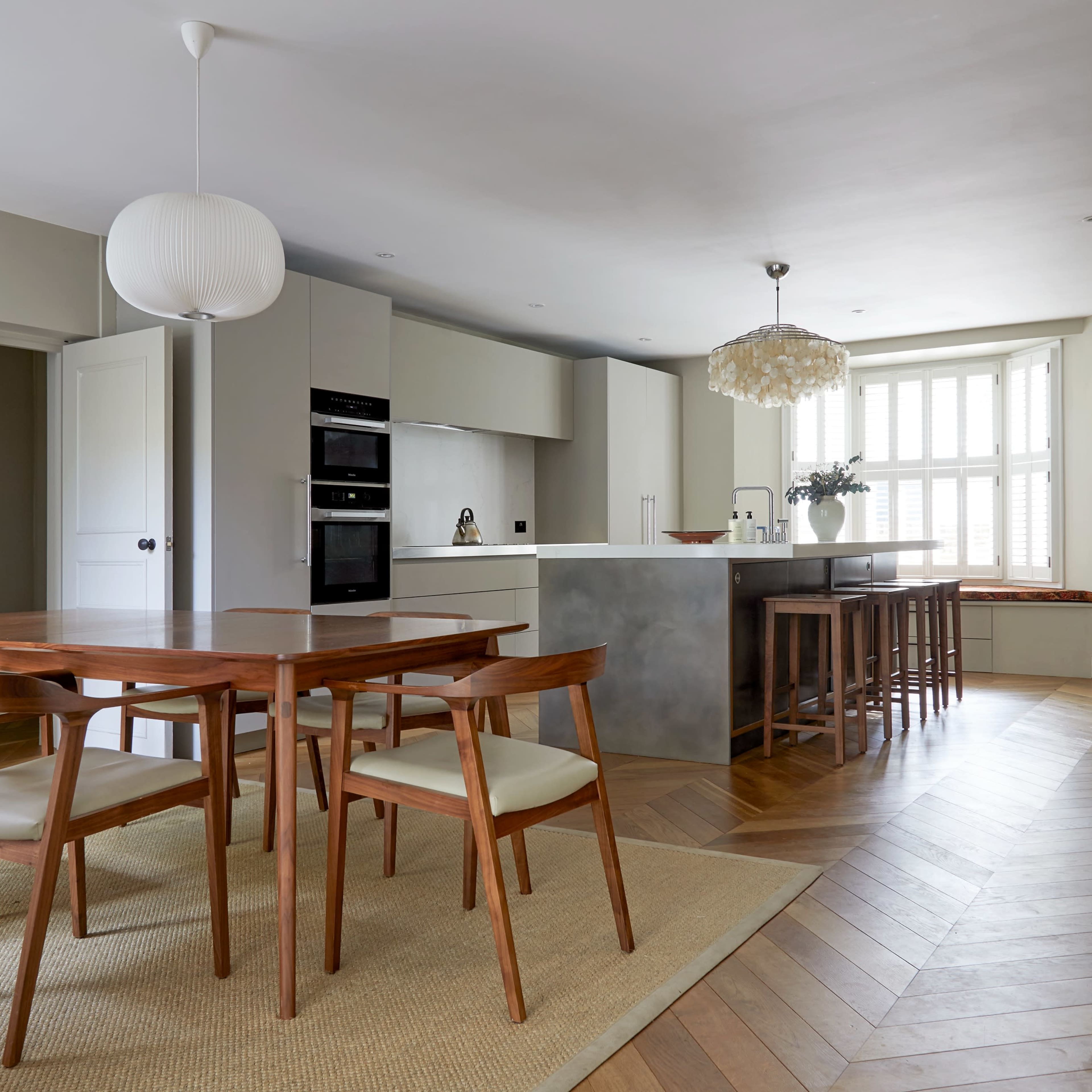 A modern kitchen dining area features a wooden table with chairs, a stylish kitchen island, and large windows allowing natural light.
