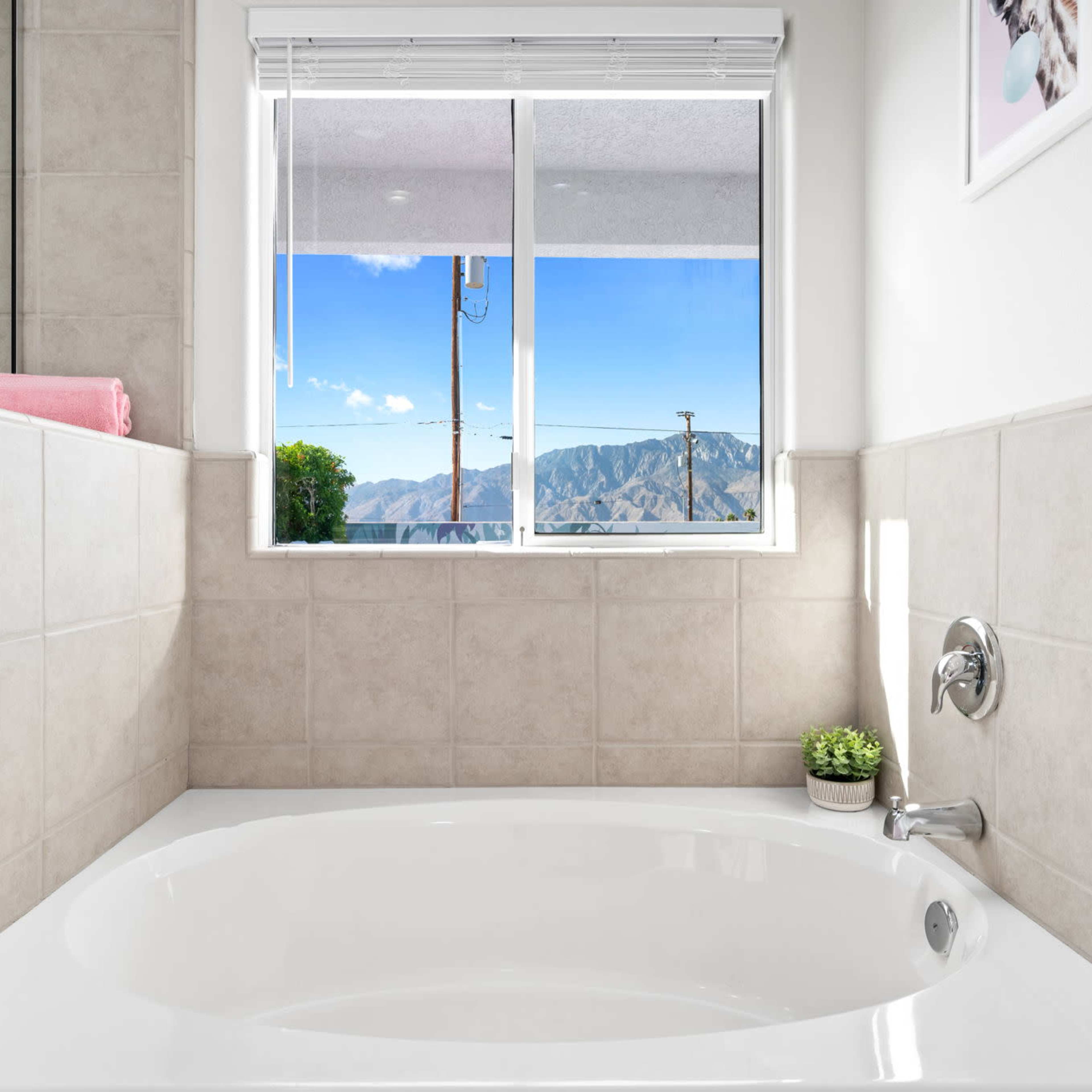 A bathroom with a white bathtub beside a window that offers a view of mountains and clear skies.