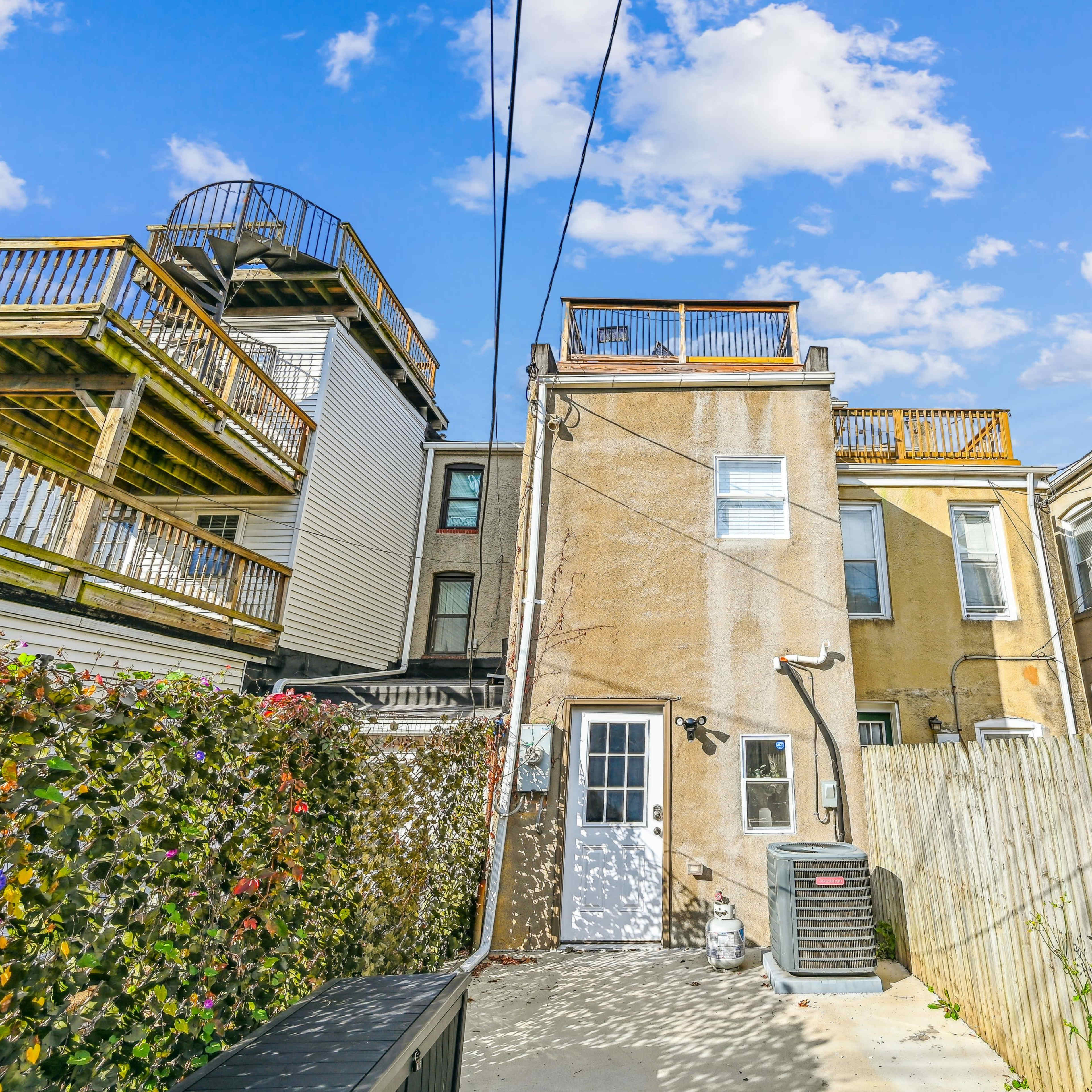 A narrow alleyway with a two-story building at the center, flanked by adjacent structures and featuring a rooftop deck above.