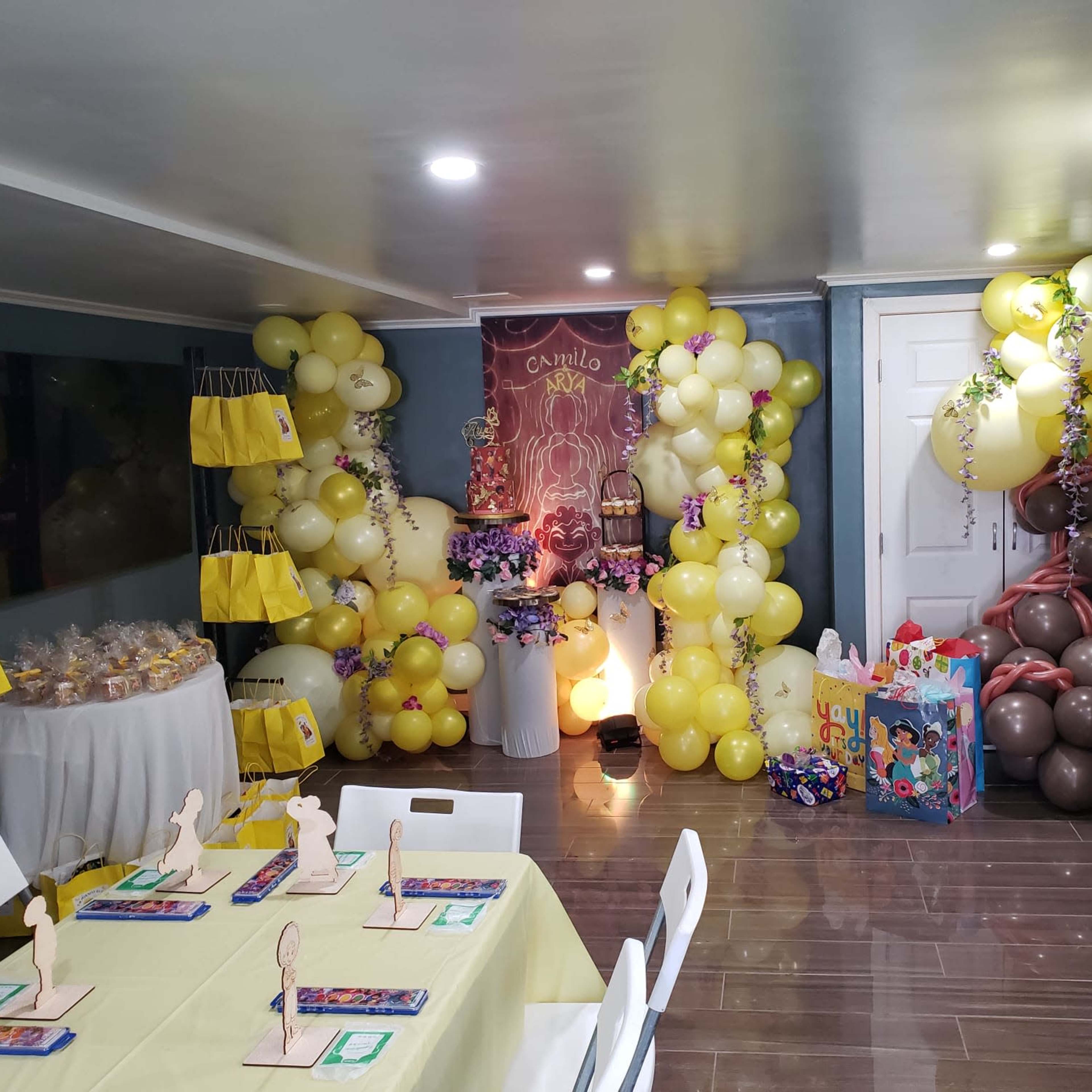 A decorated room for a party, featuring colorful balloons, a table set with place cards, and party favors arranged on a table.
