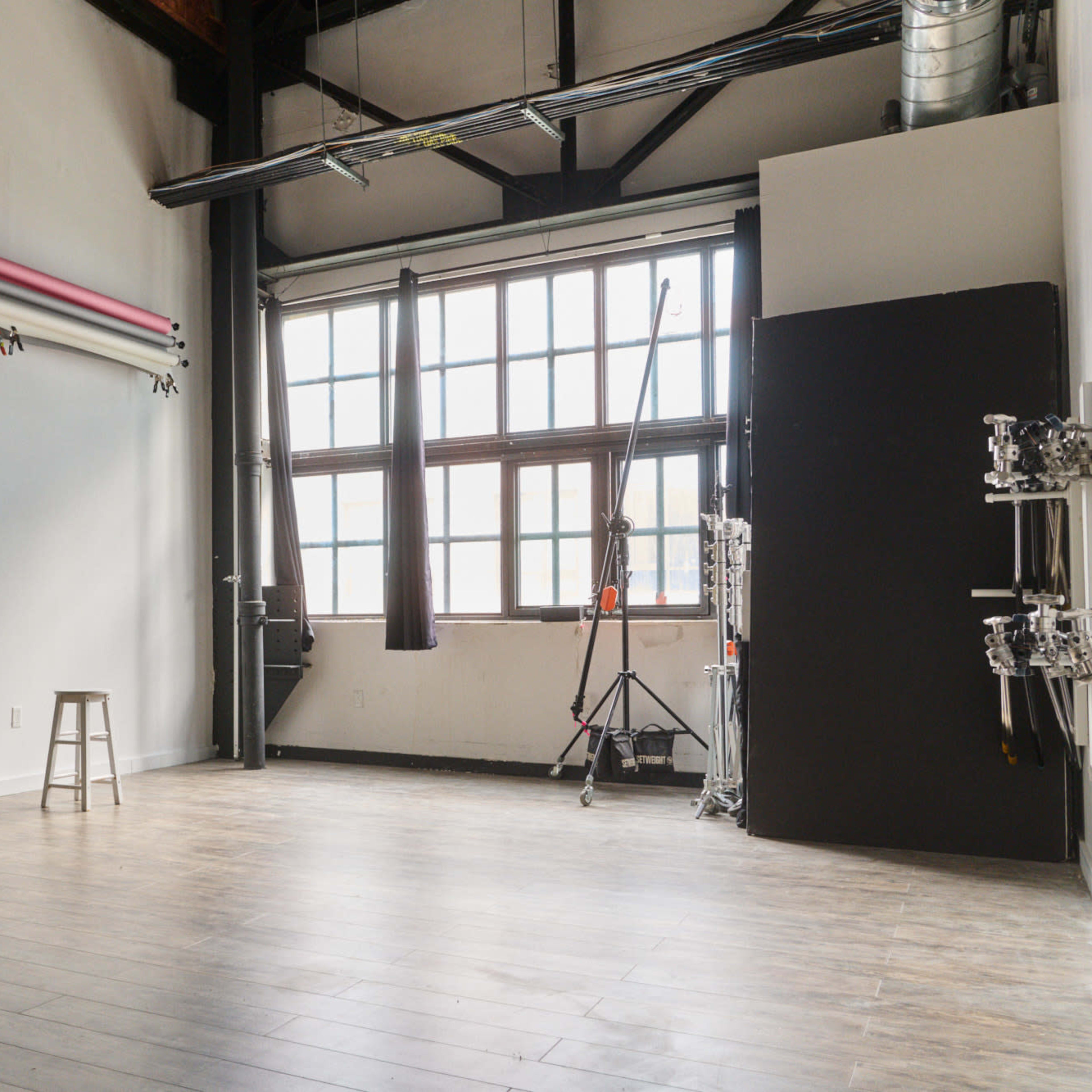 An empty photography studio with colorful backdrops on one wall and large windows allowing natural light in.