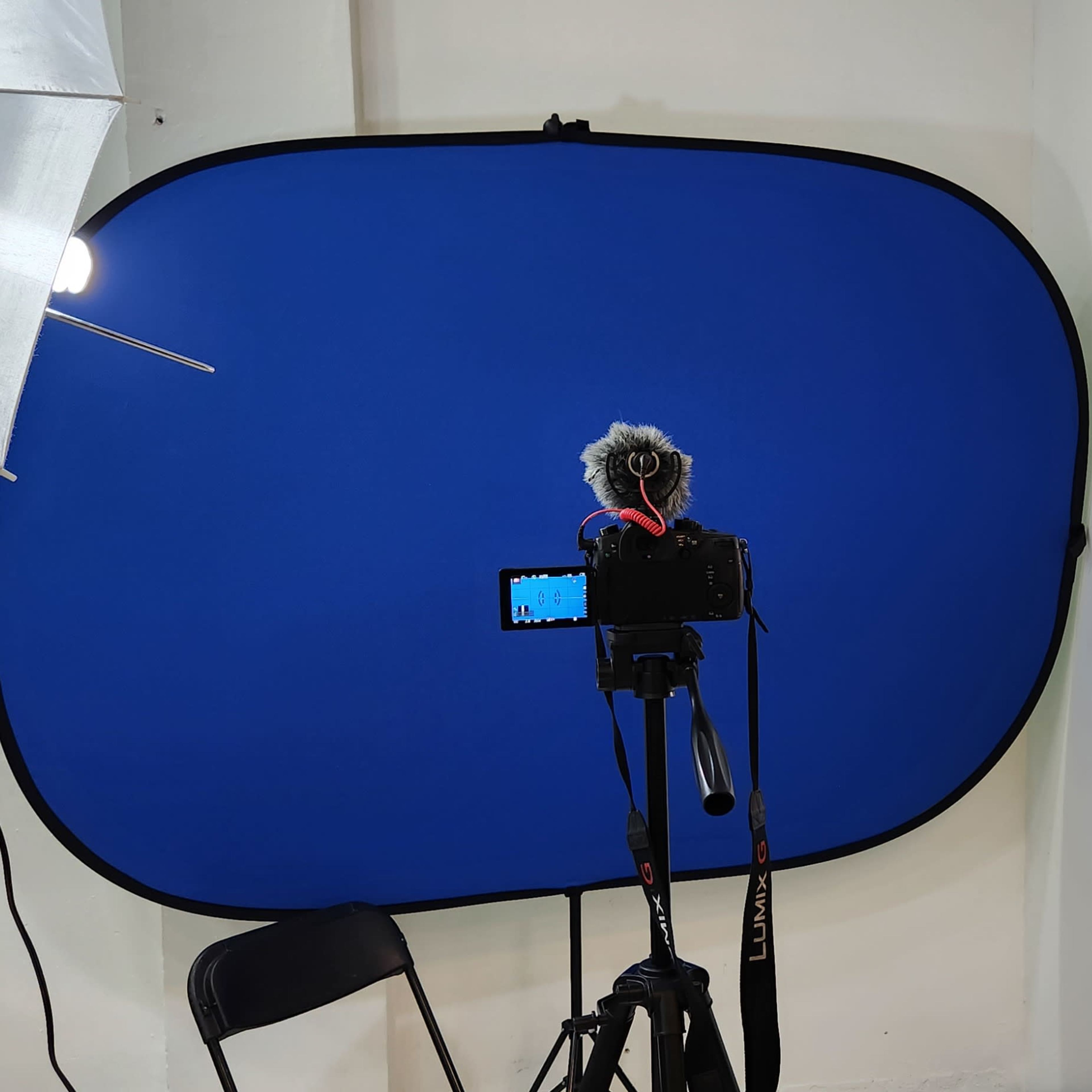 A photography setup with a blue backdrop, a camera on a tripod, a microphone, and lighting equipment.