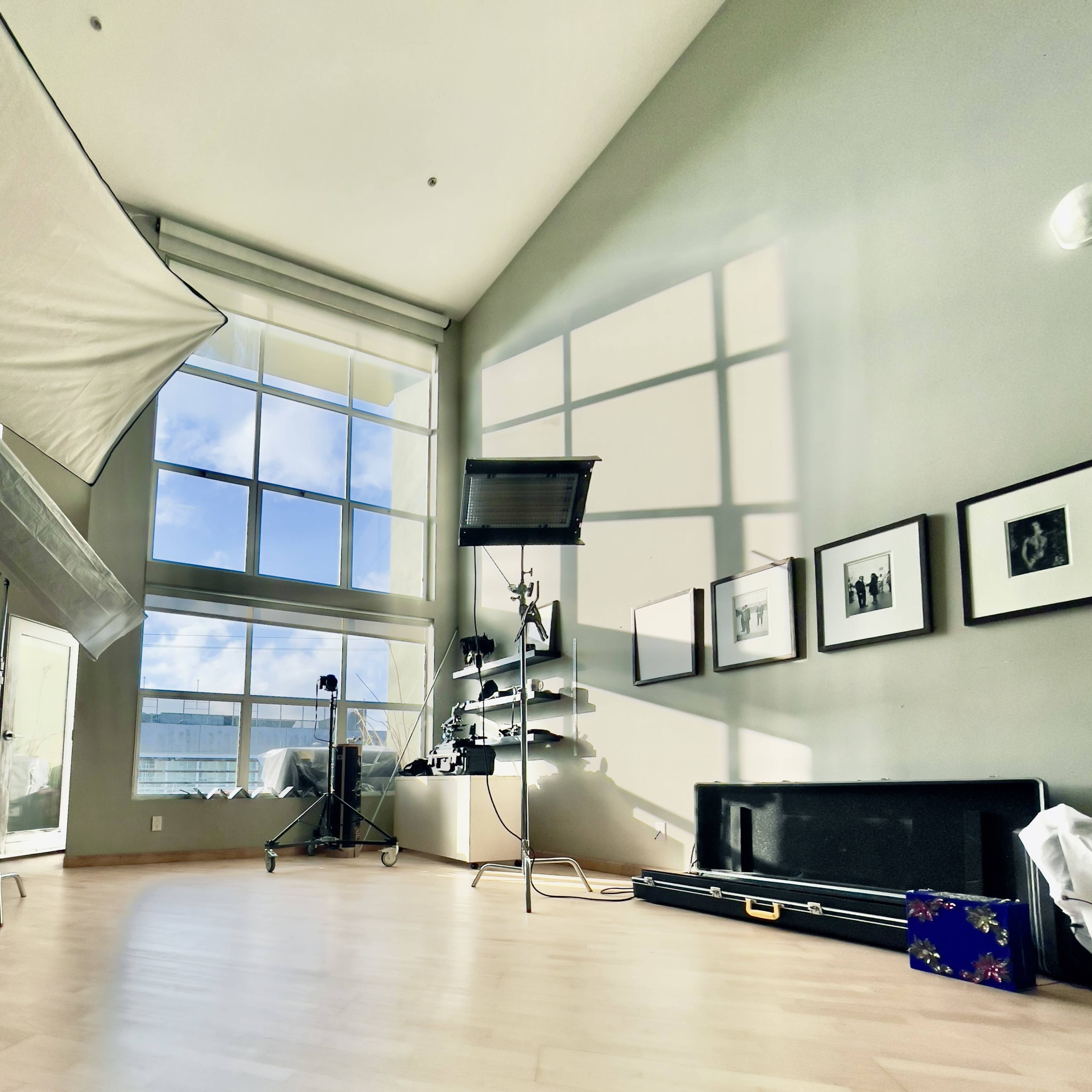 A spacious room with large windows, a lighting setup, and various framed photographs on the wall.