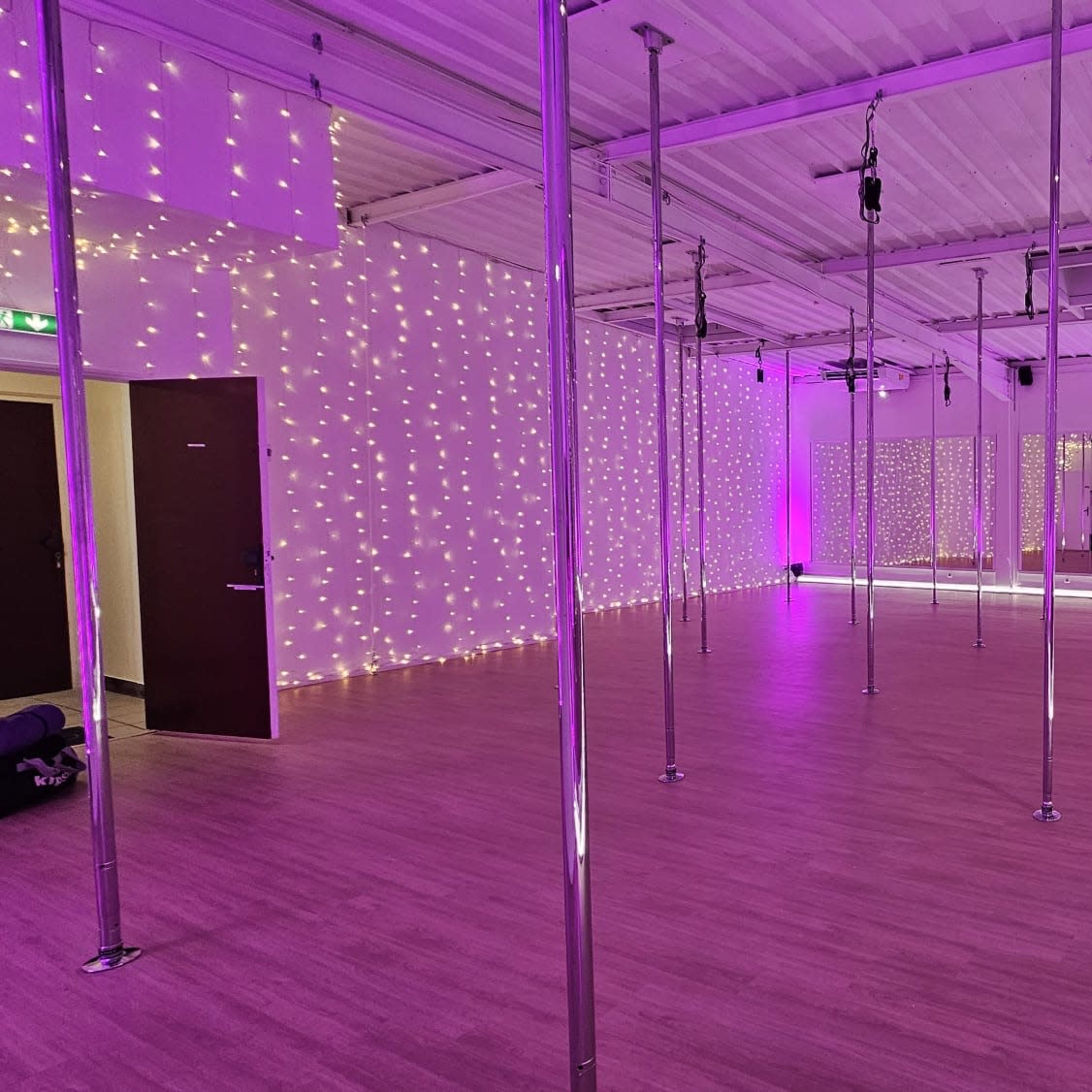 A brightly lit pole dancing studio with mirrored walls and purple ambient lighting.