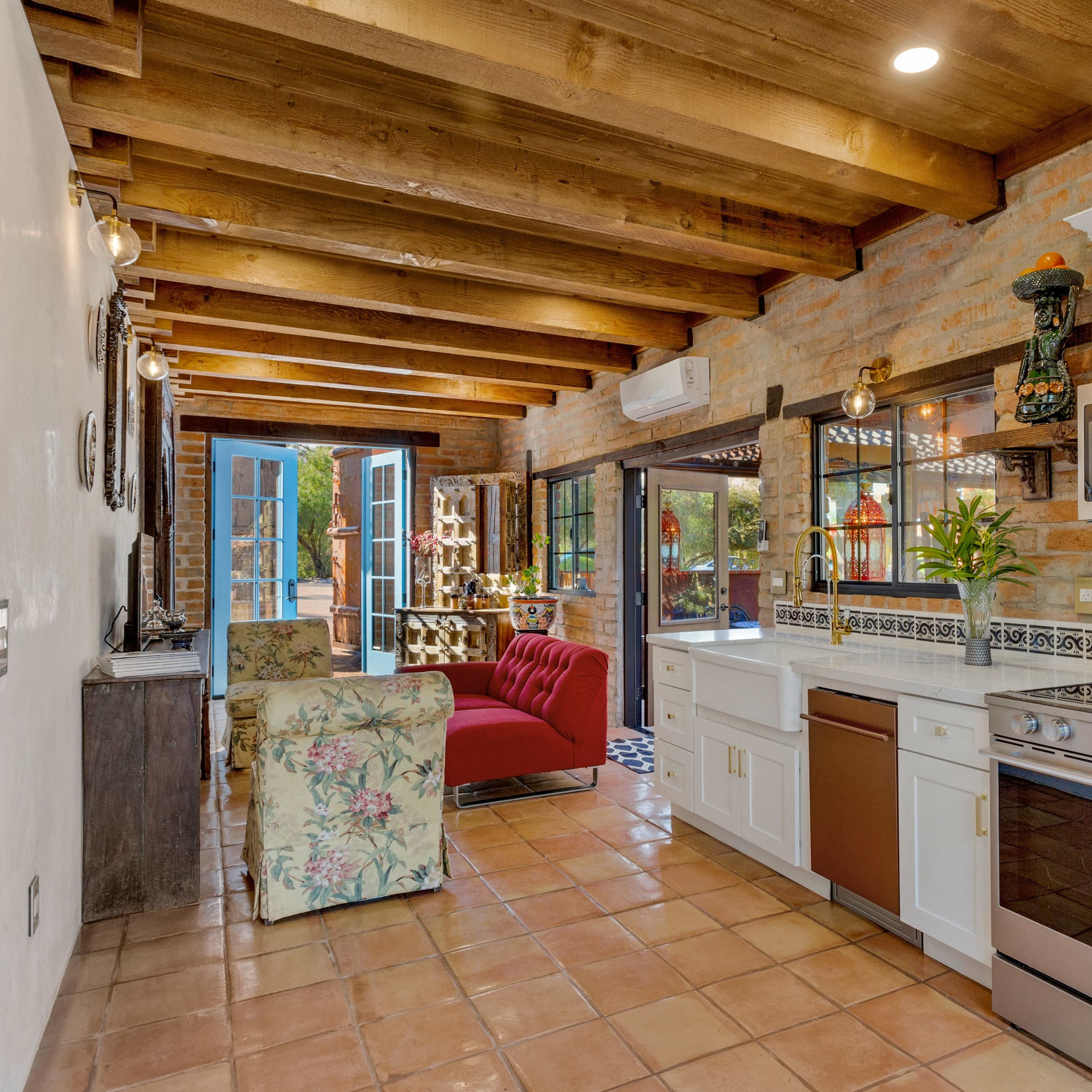 A kitchen with white cabinets, stainless steel appliances, and a red chair in a rustic setting featuring exposed wooden beams and a tile floor.