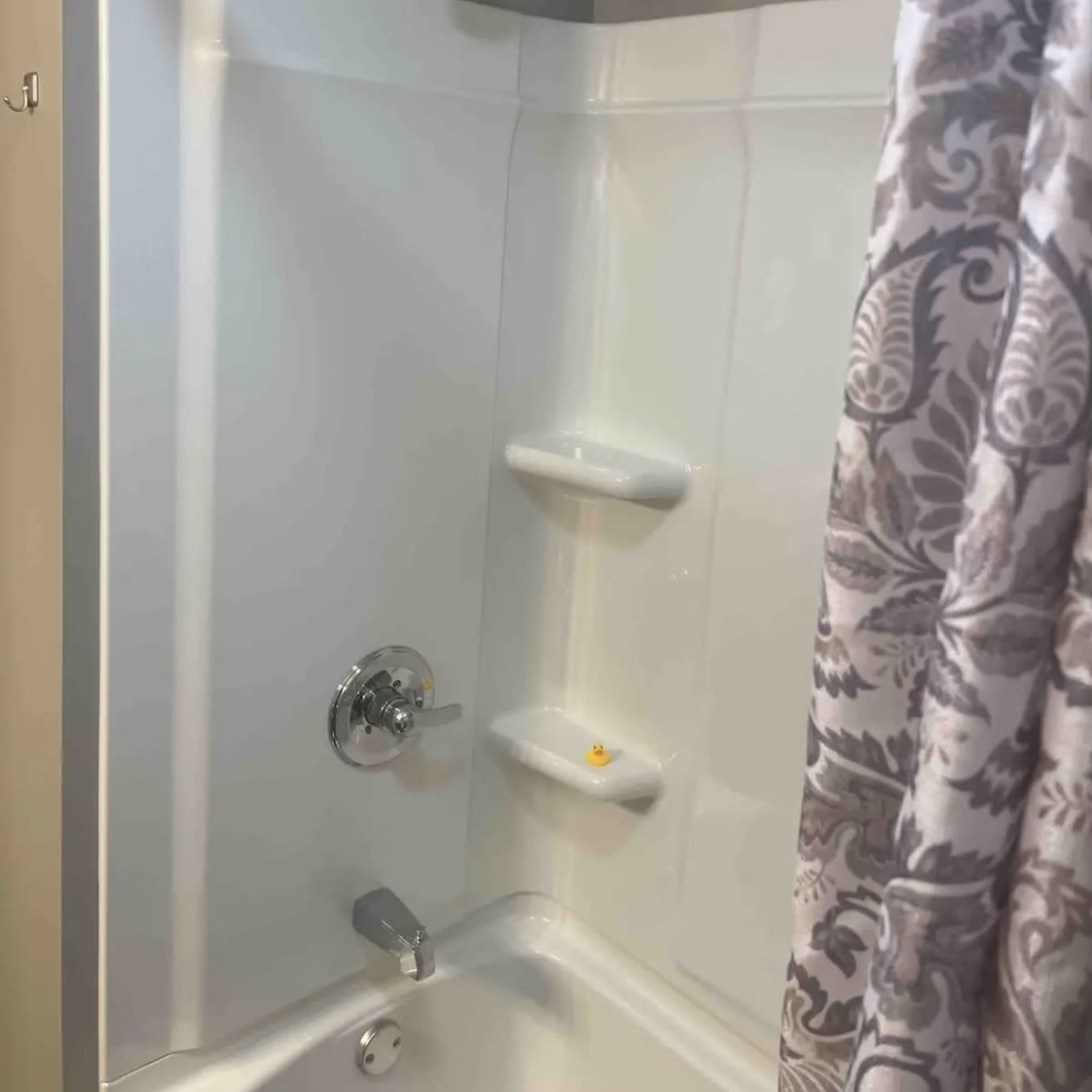 A clean shower area with a silver showerhead, a wall-mounted faucet, and a patterned curtain hanging to the side.