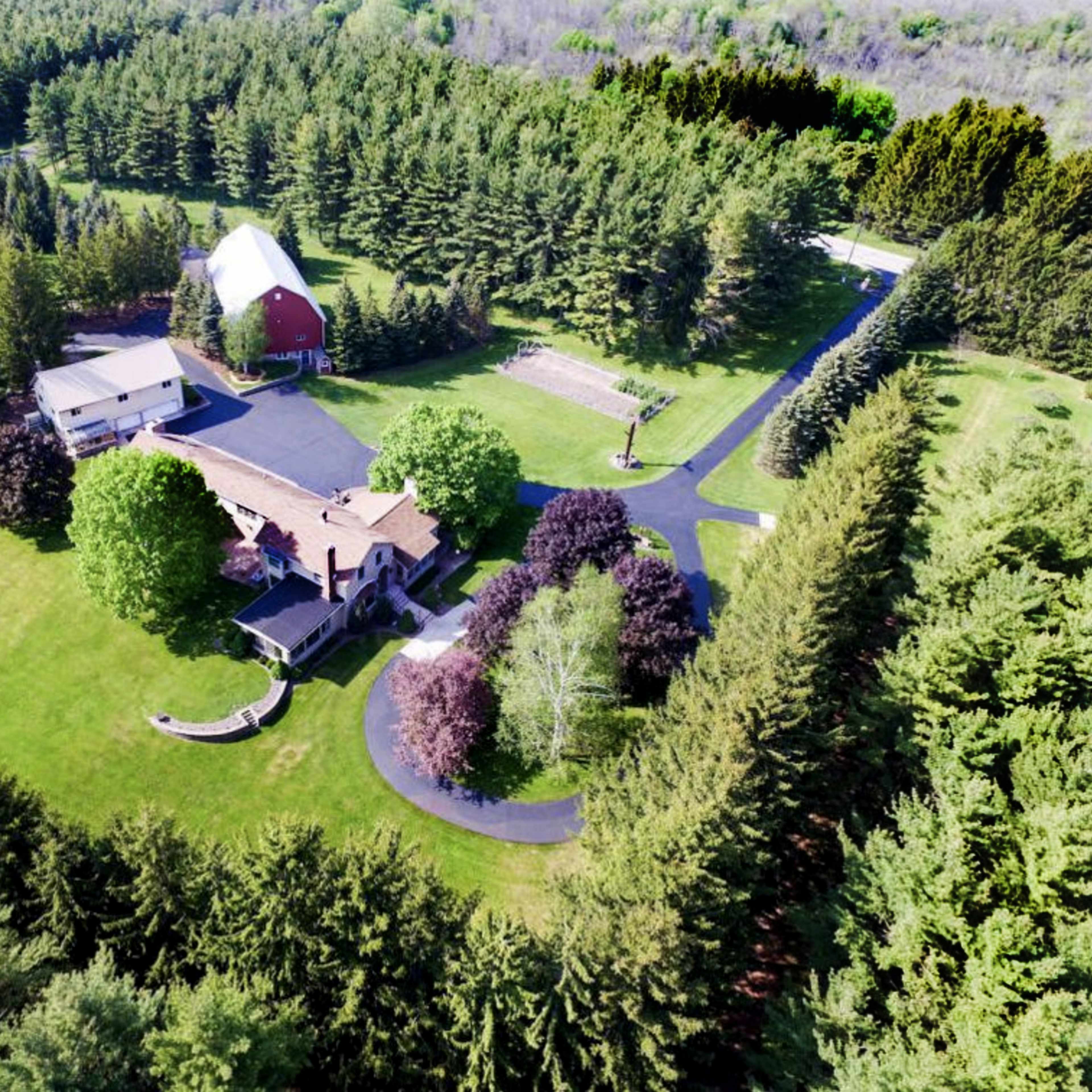 An aerial view of a large property with a main house, a barn, and several trees surrounding a well-maintained lawn.