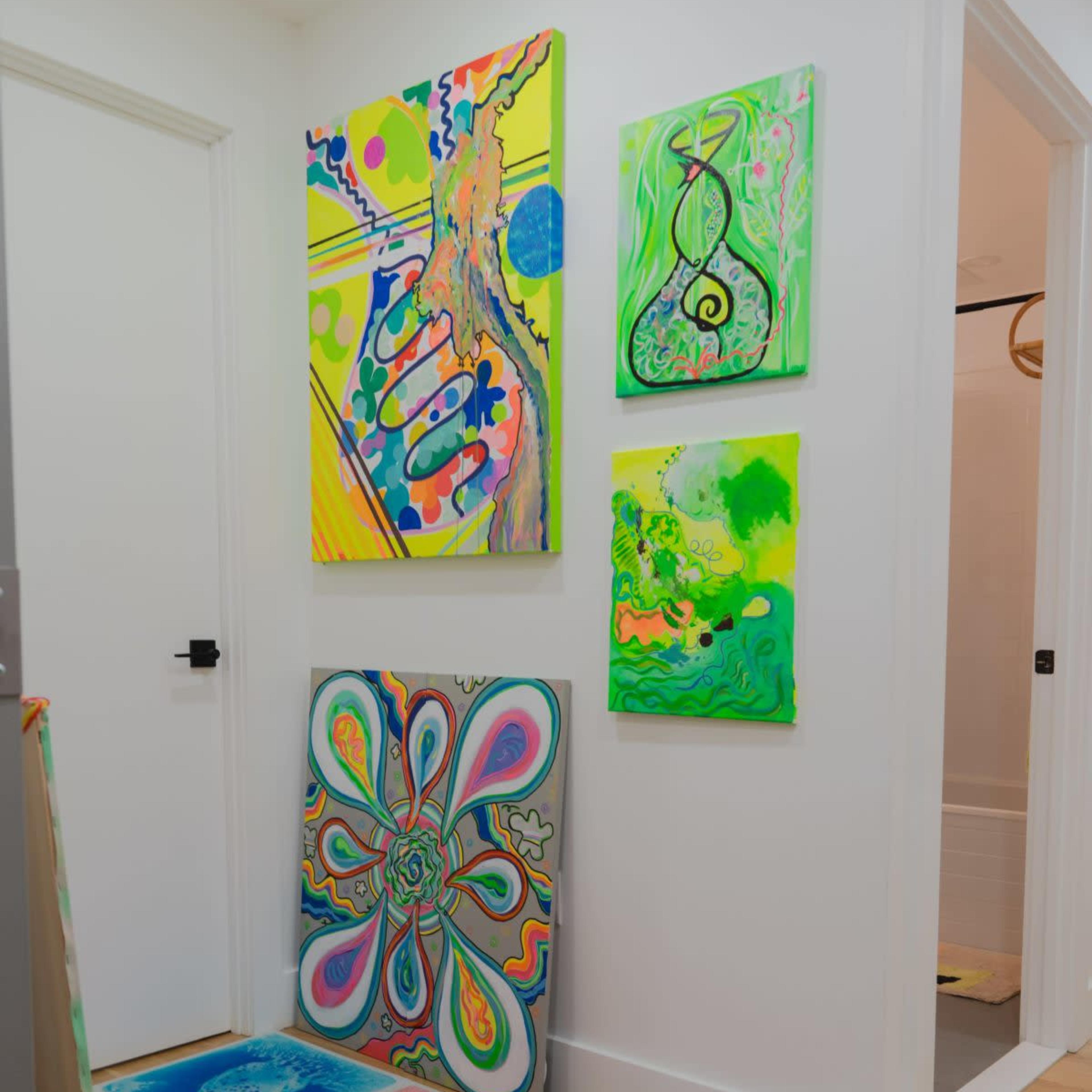A hallway featuring several brightly colored abstract paintings on the walls and a collection of vibrant art pieces arranged on the floor.