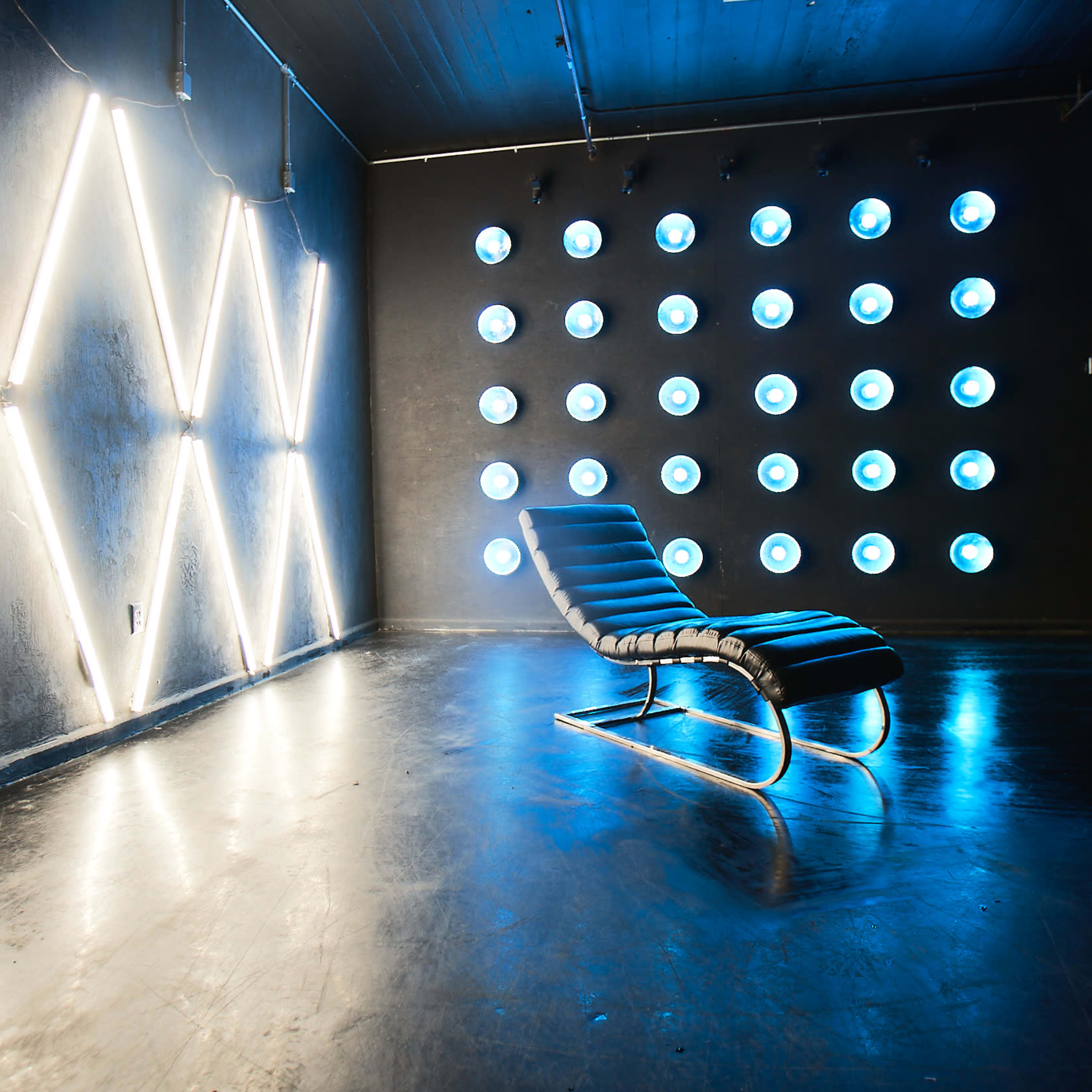 A modern lounge chair in a dimly lit room illuminated by neon lights and circular light fixtures on the wall.