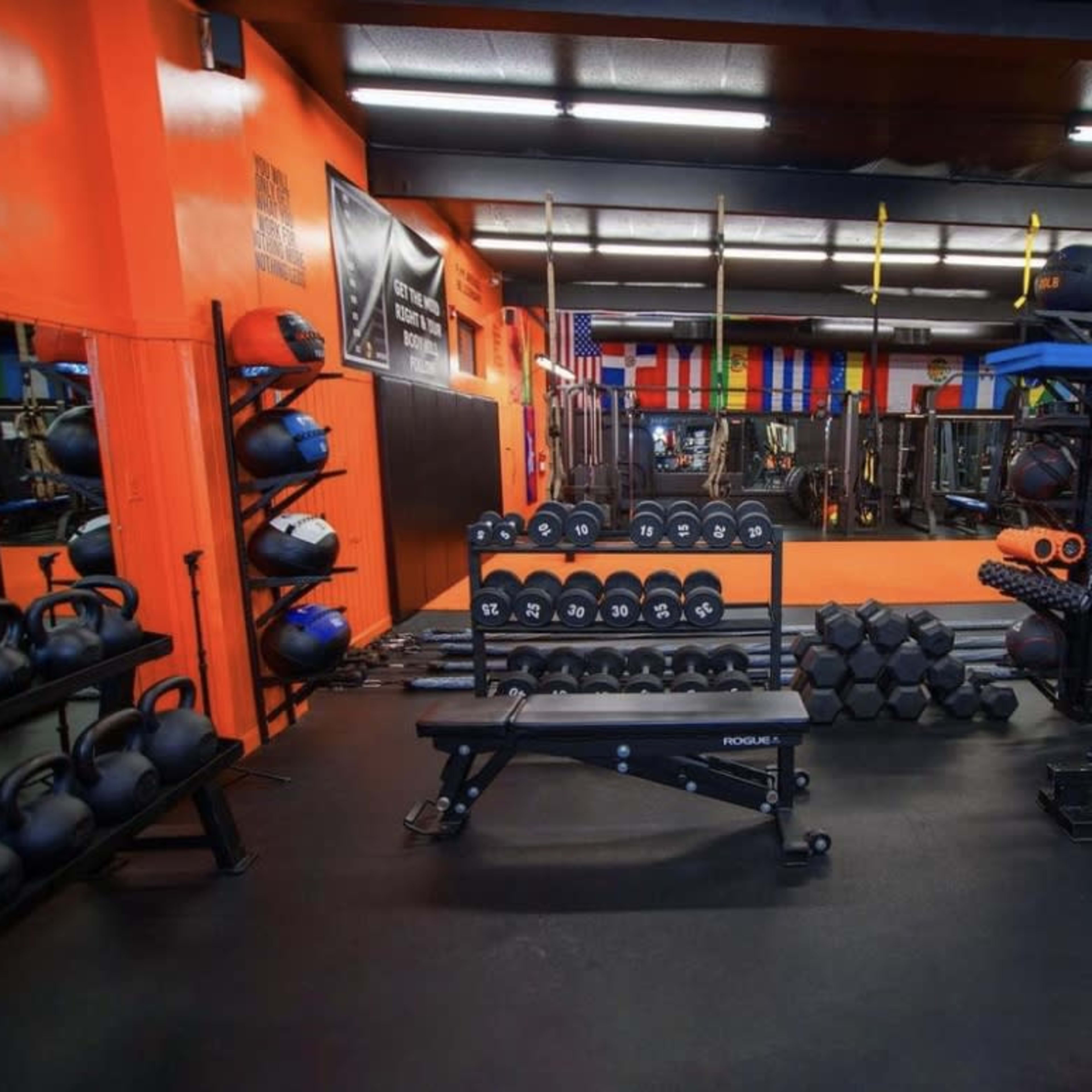 A fitness gym with various weights, kettlebells, and exercise equipment arranged on the floor against brightly colored walls and mirrors.