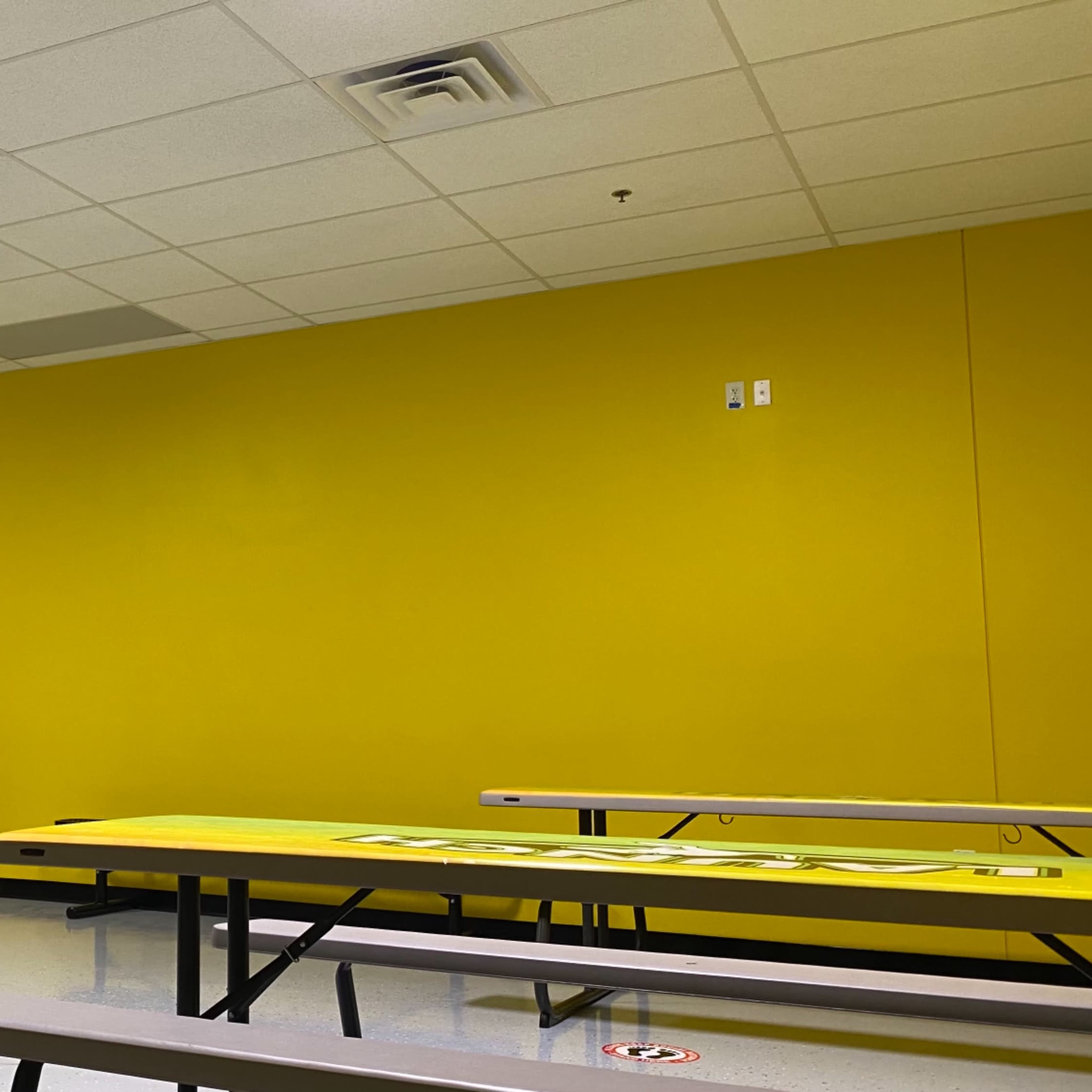 A room with bright yellow walls, several gray tables, and a linoleum floor.